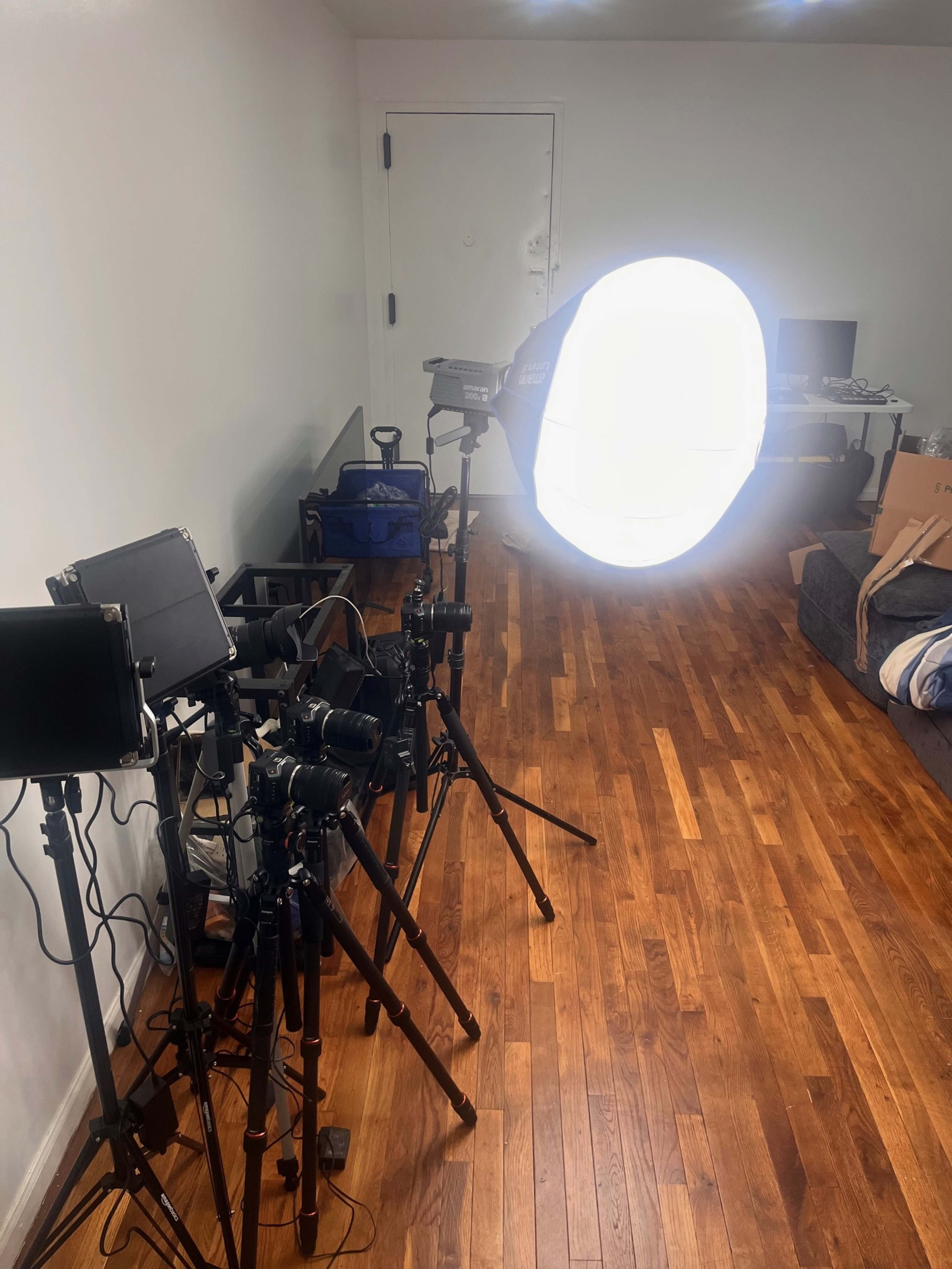 A photography setup is arranged in a room, featuring multiple cameras, lighting equipment, and a backdrop.