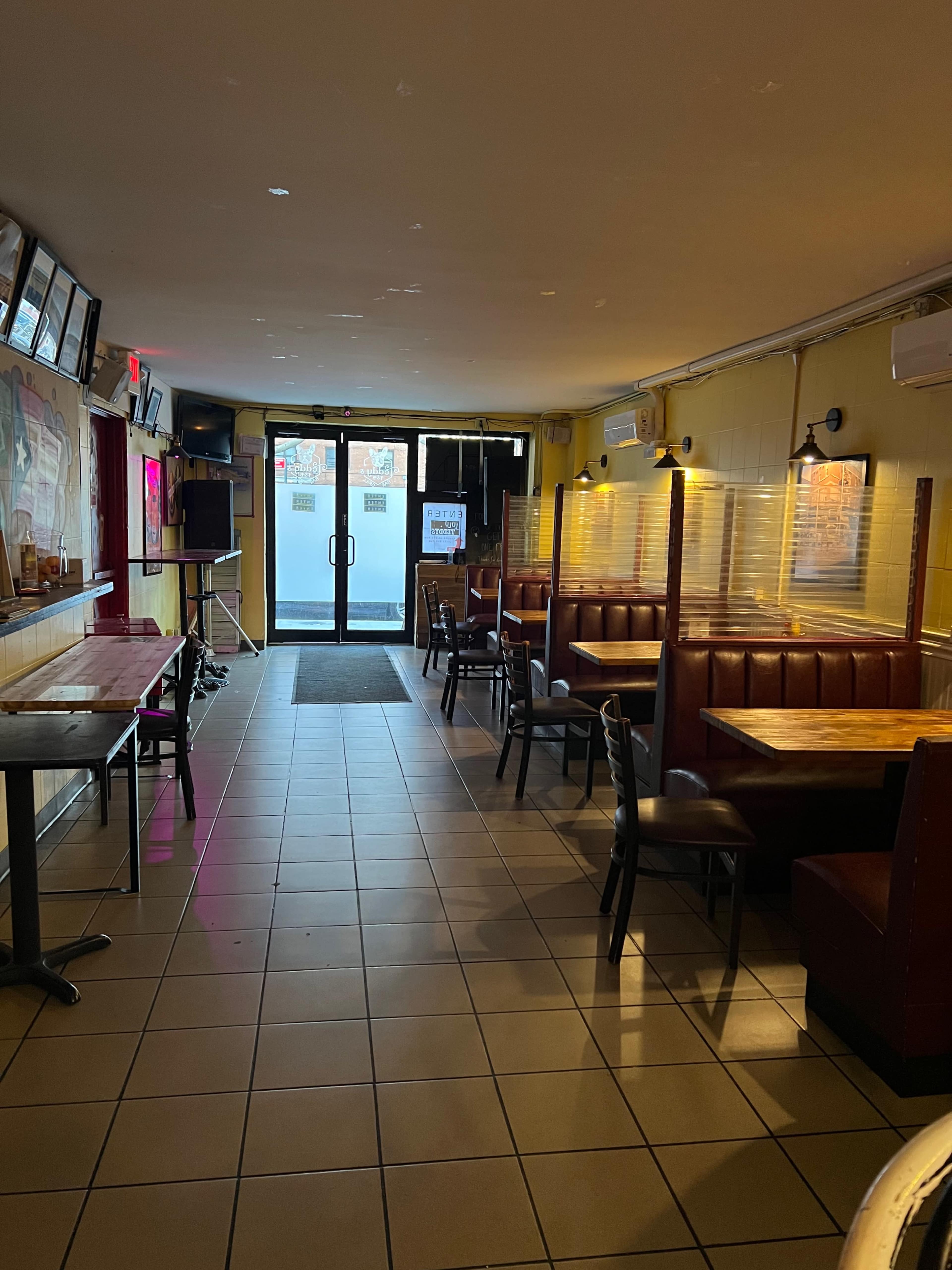 A partially empty restaurant interior featuring booths on one side and tables on the other, with a glass door at the far end leading outside.