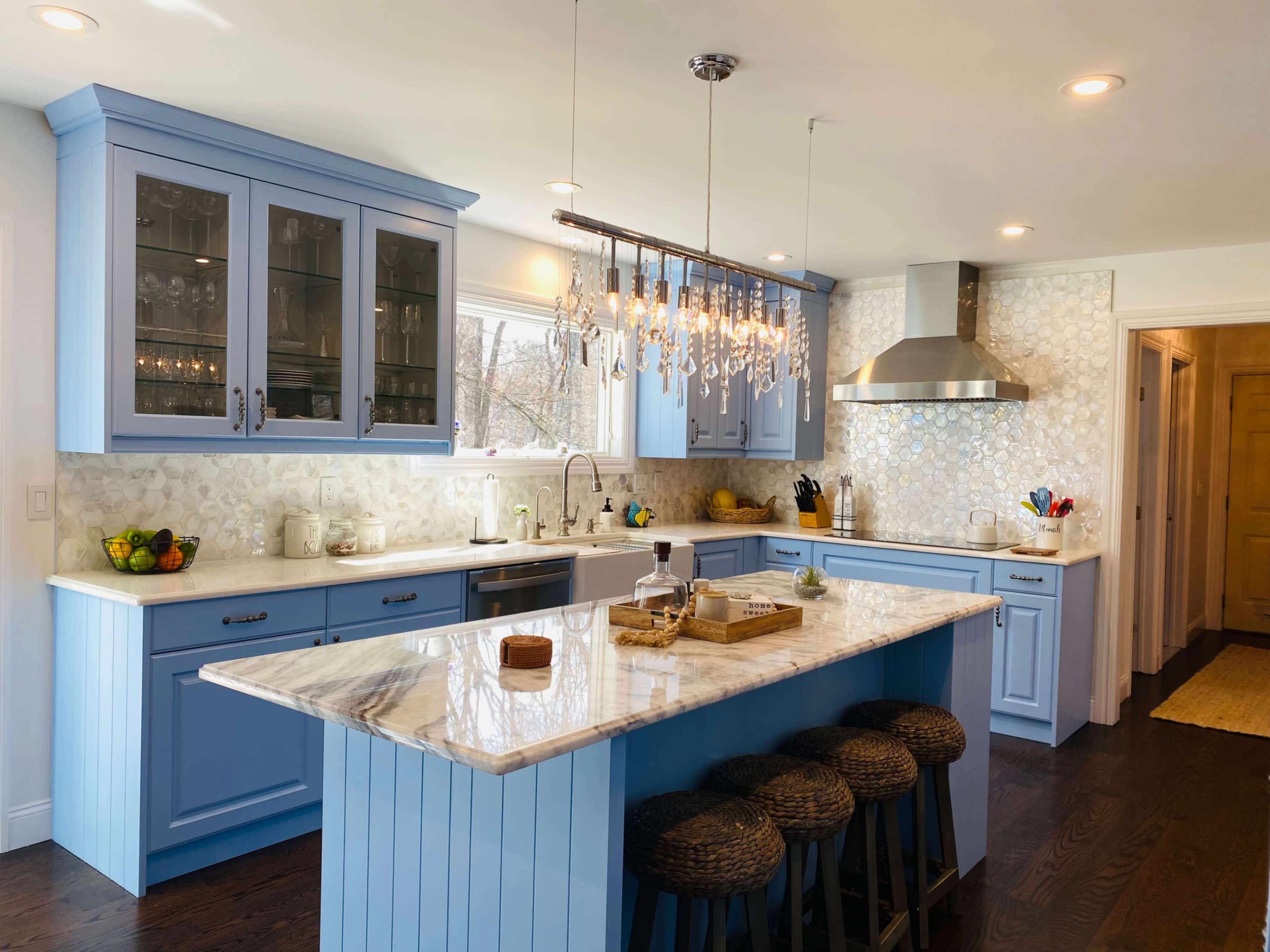The kitchen features blue cabinetry, a marble island with bar stools, and a chandelier above, with a modern stainless steel range and backsplash.