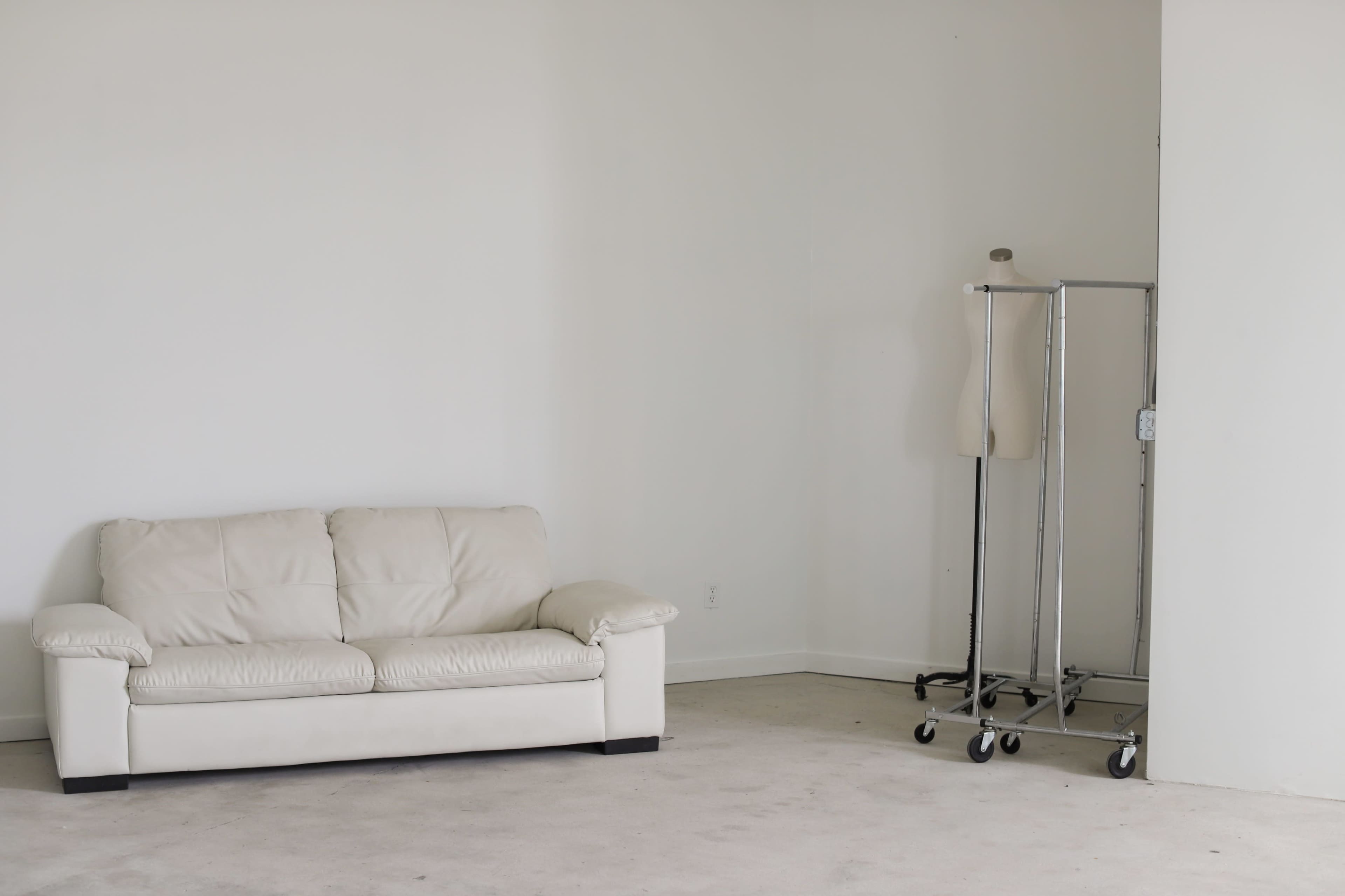 A beige sofa sits against a plain wall, with a clothing rack and a mannequin positioned nearby.