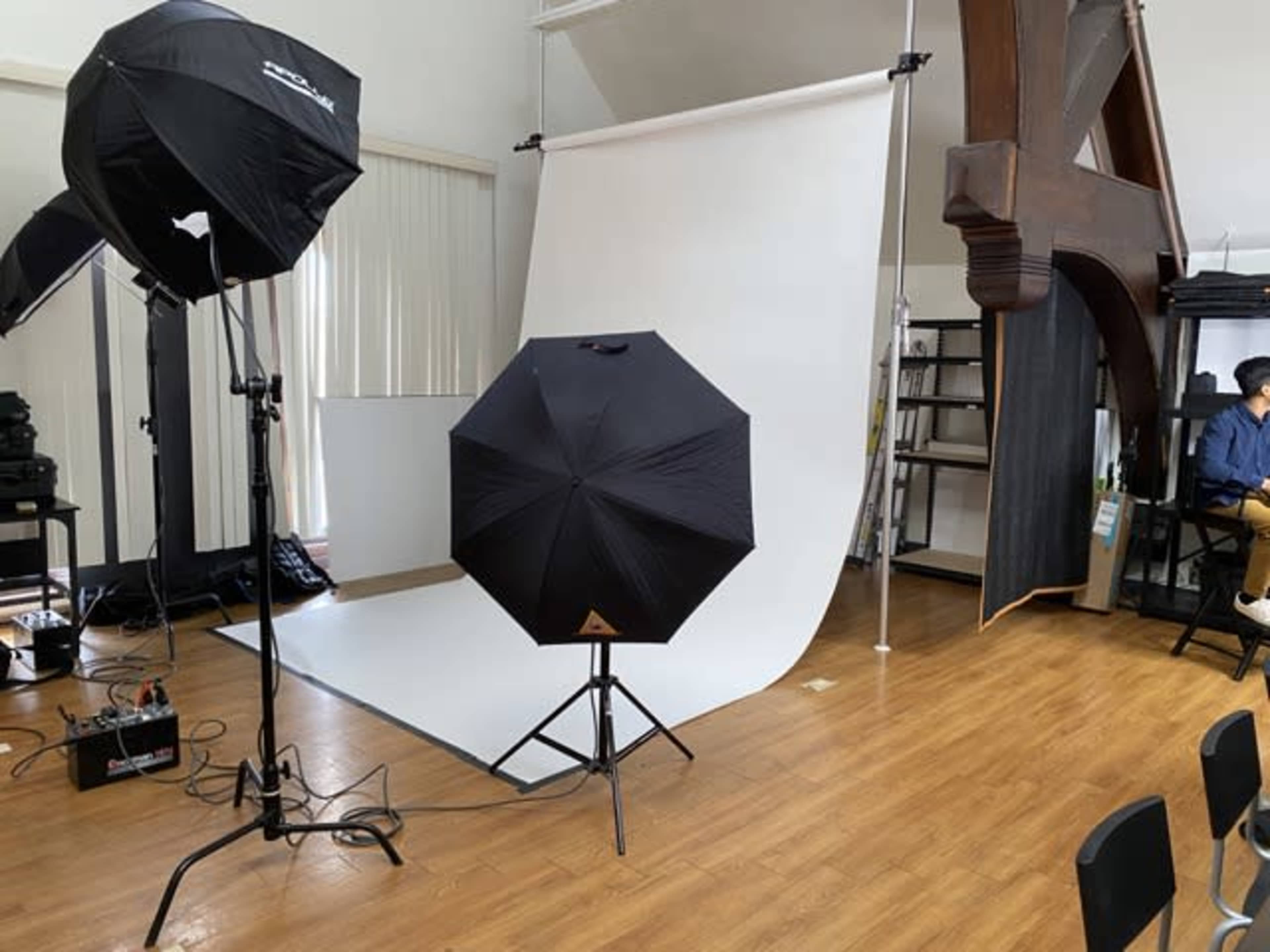 A photography studio setup with multiple light umbrellas, a white backdrop, and a wooden support structure.