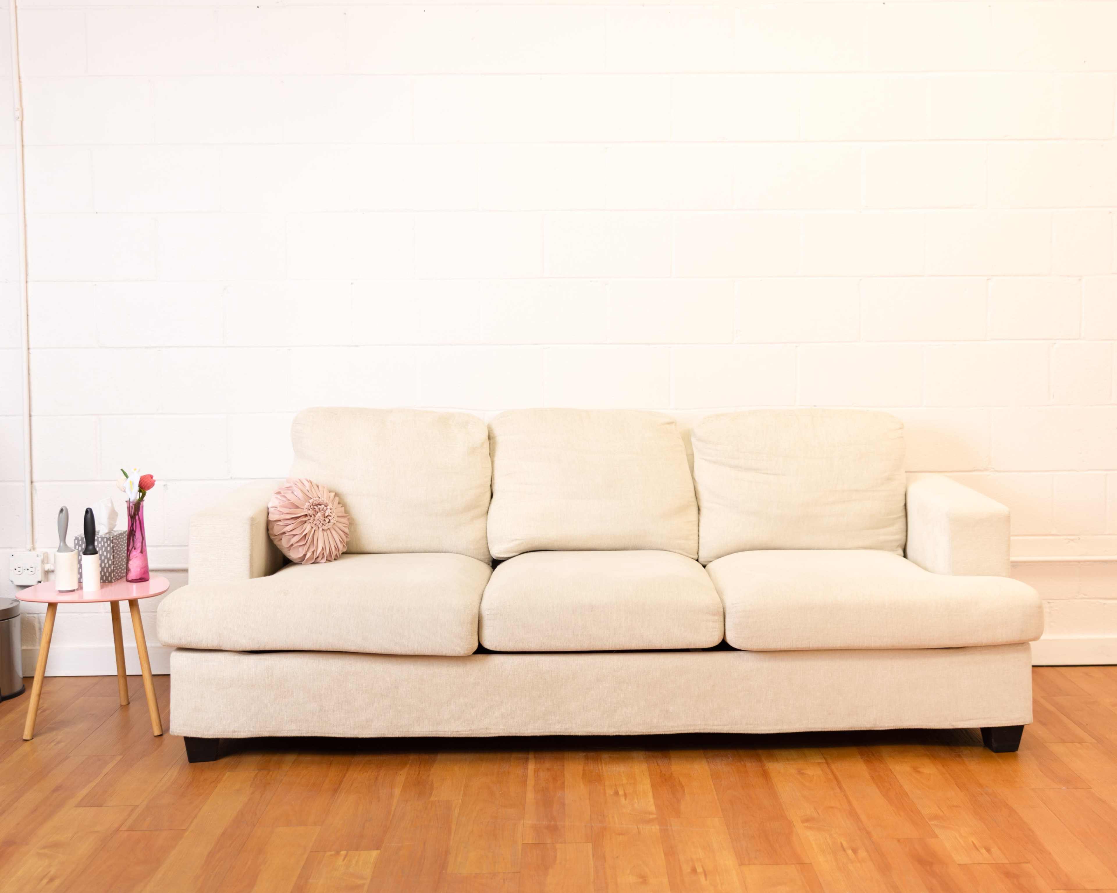 A beige three-seat sofa is positioned against a white wall, accompanied by a small pink table holding decorative items.