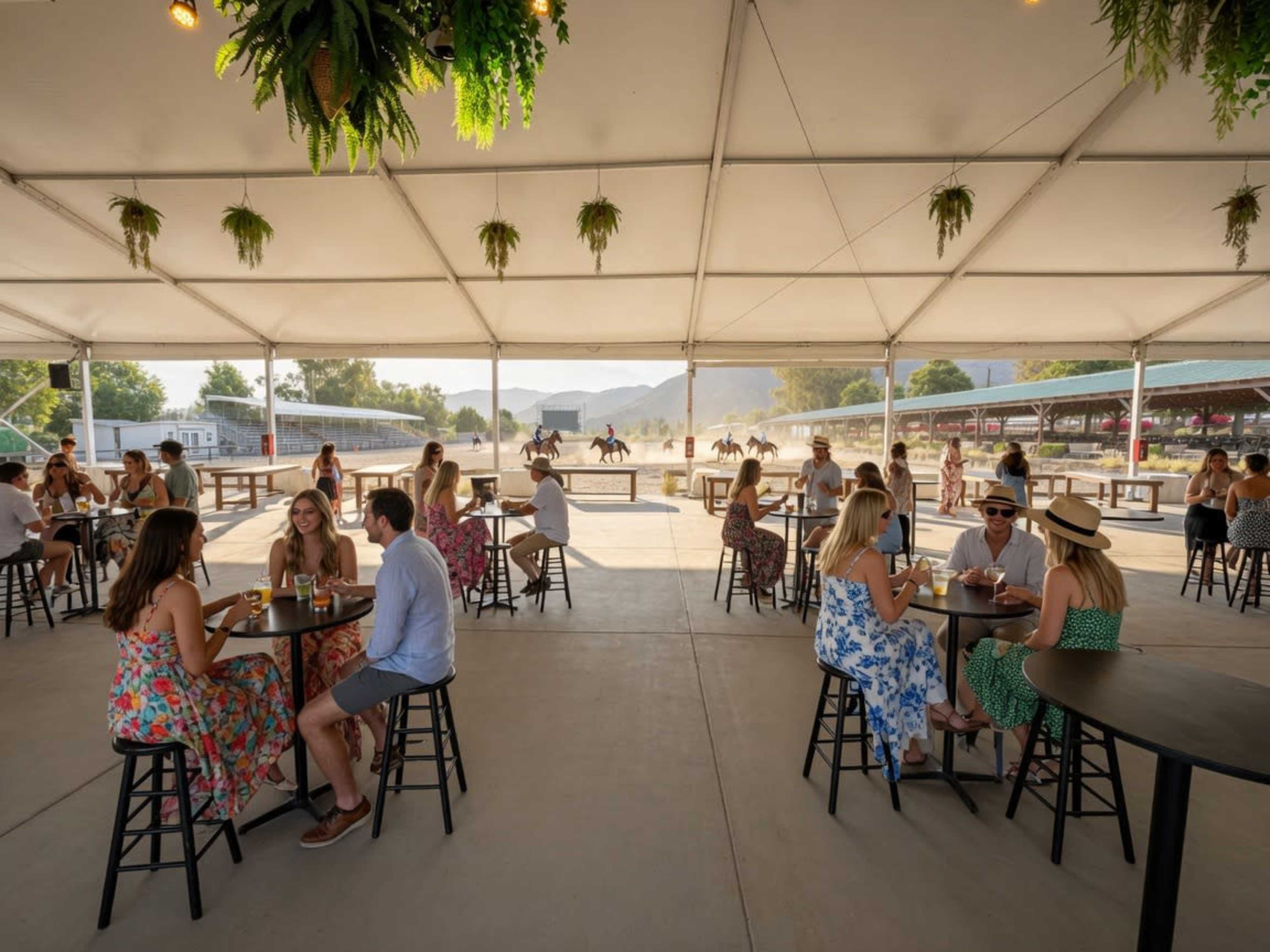 A large tent with seated guests at tables overlooks riders on horseback in an outdoor setting.