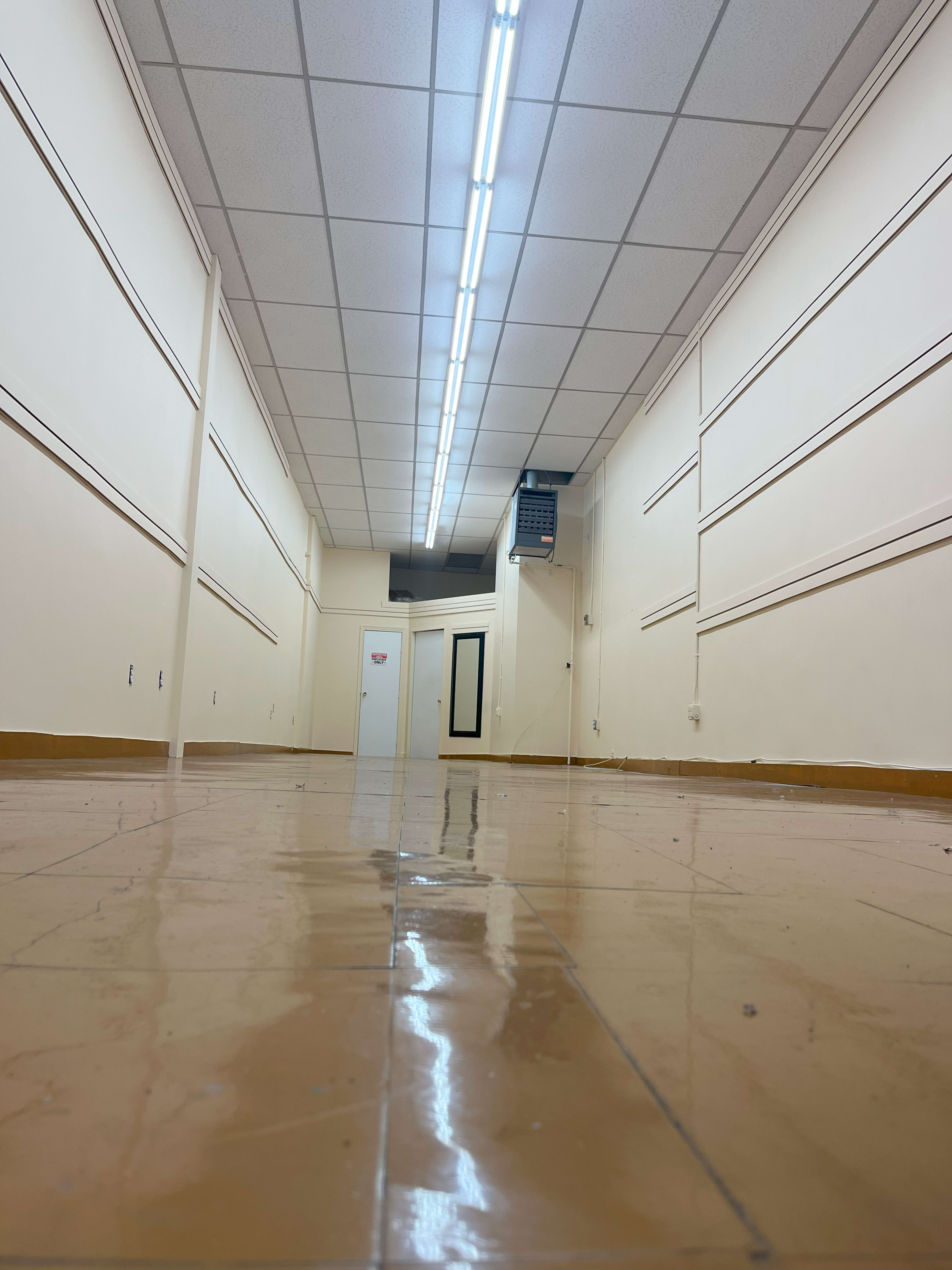 A long, empty hallway with polished tile floors and fluorescent lighting overhead.