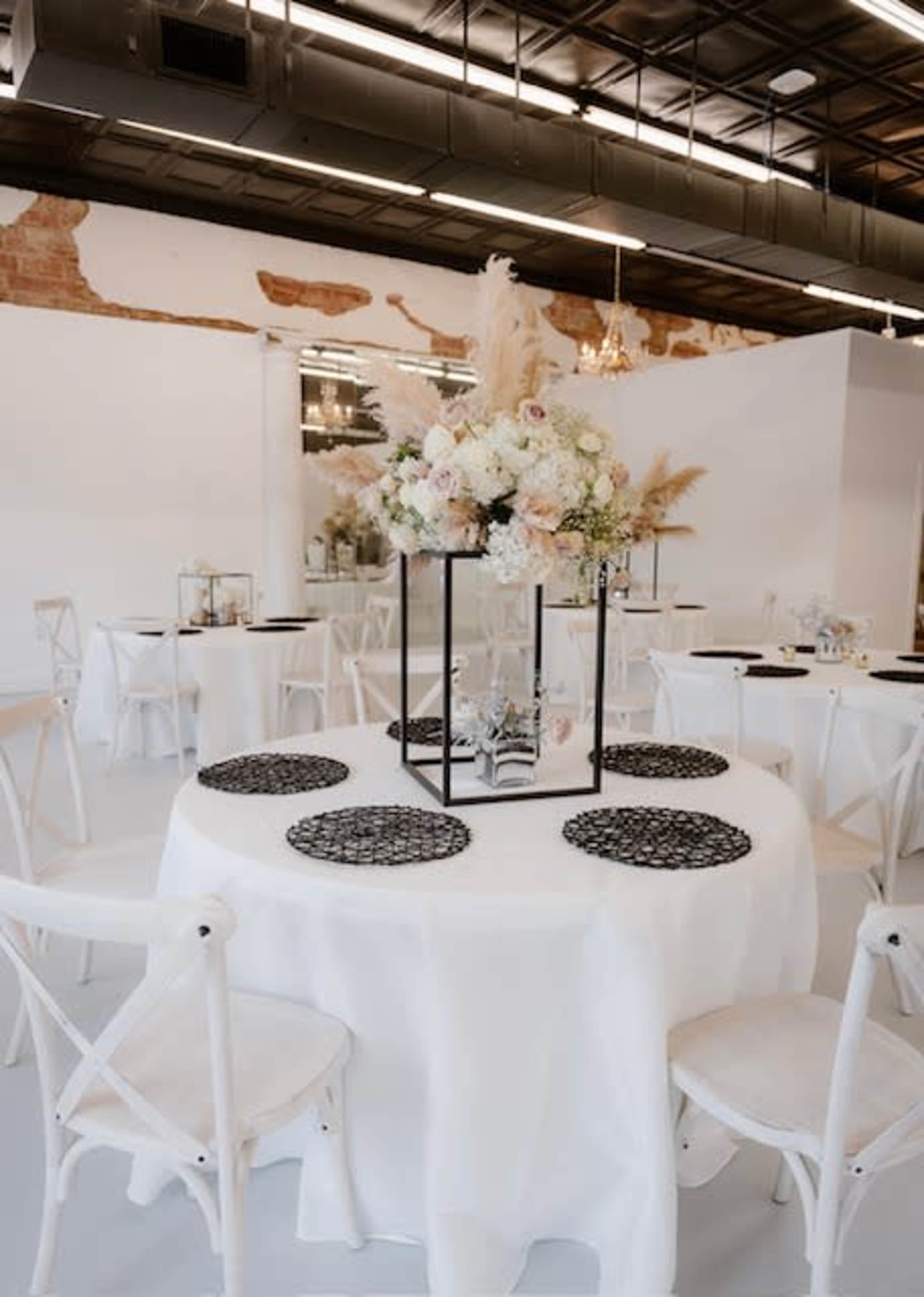 A modern banquet hall set with round tables covered in white tablecloths, featuring floral centerpieces and decorative place settings.