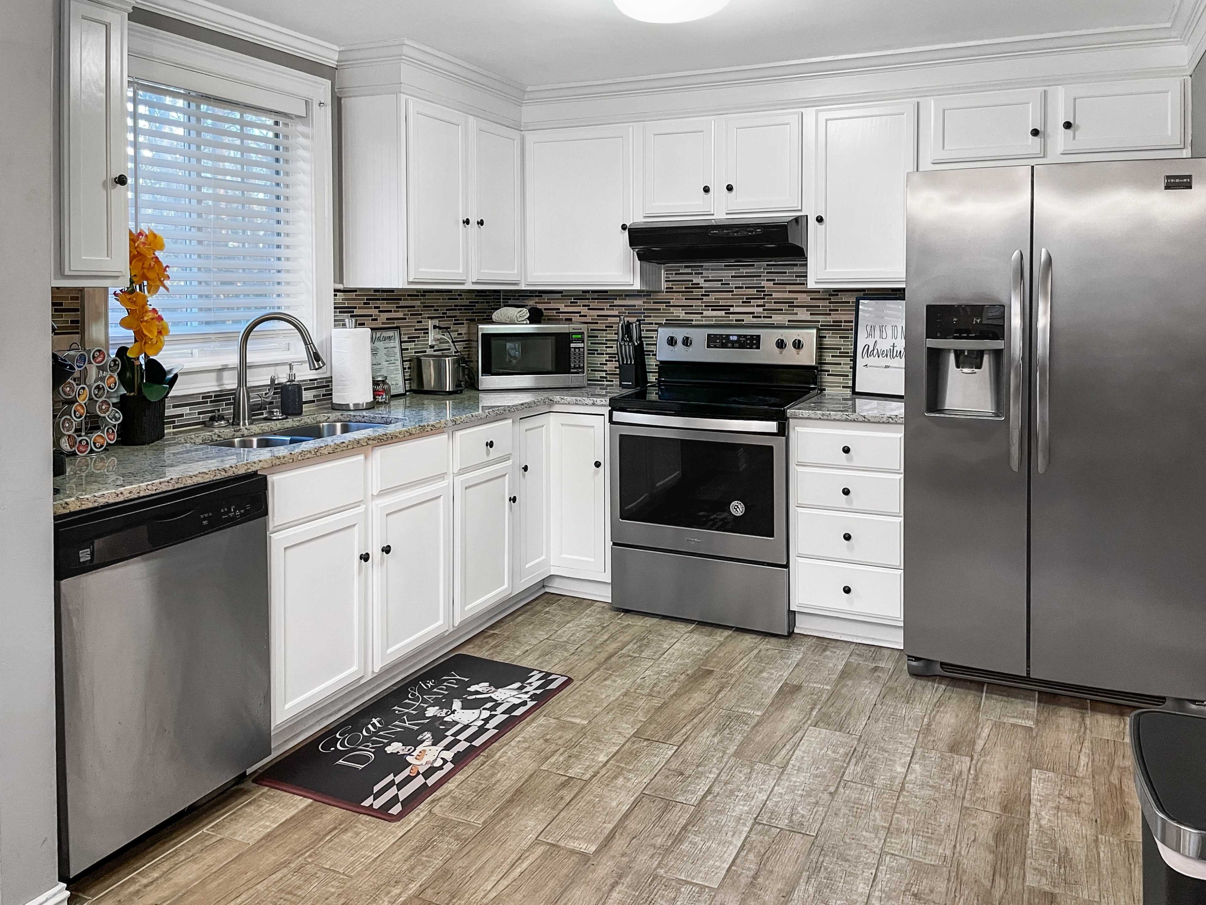 A modern kitchen features white cabinets, stainless steel appliances, a granite countertop, and a tiled backsplash.