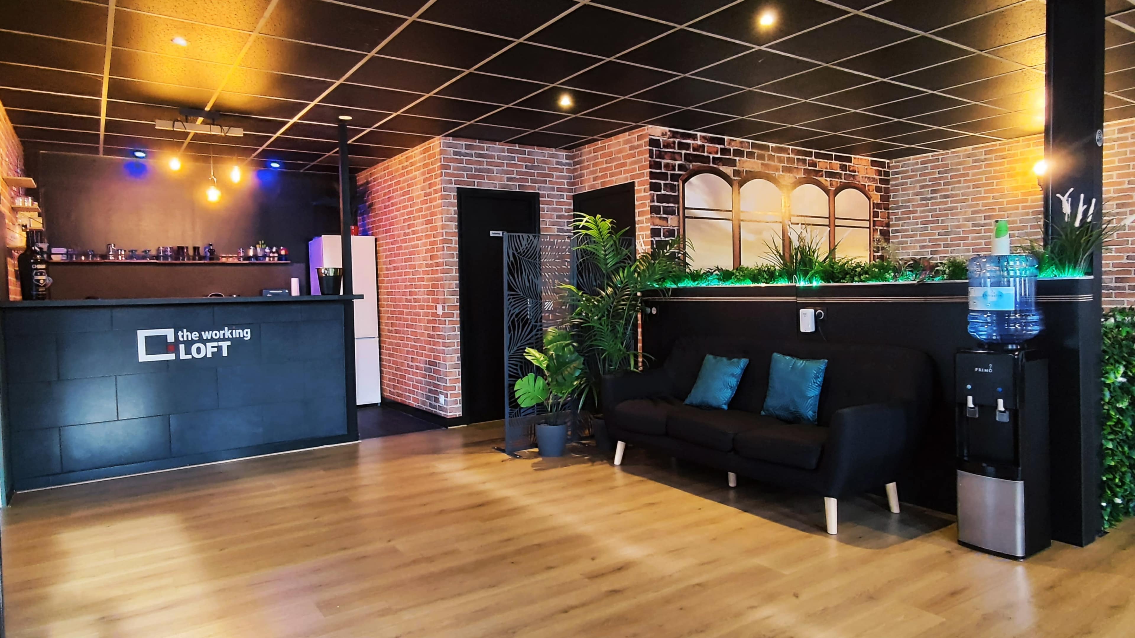 A modern office lobby with a reception area, seating, brick walls, and plants, featuring a water cooler and counter.