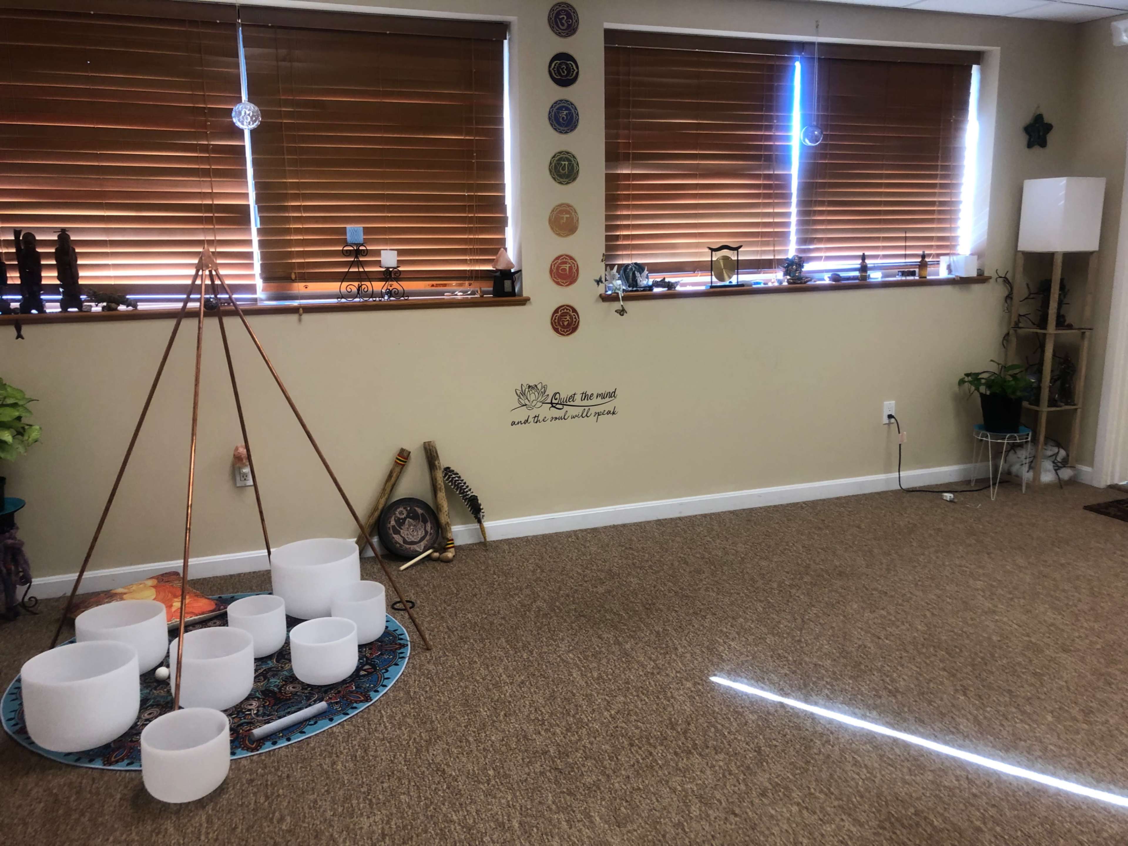 The room features a set of white singing bowls arranged on a decorative mat, with wooden blinds covering the windows and various decorative items displayed on the walls and shelves.