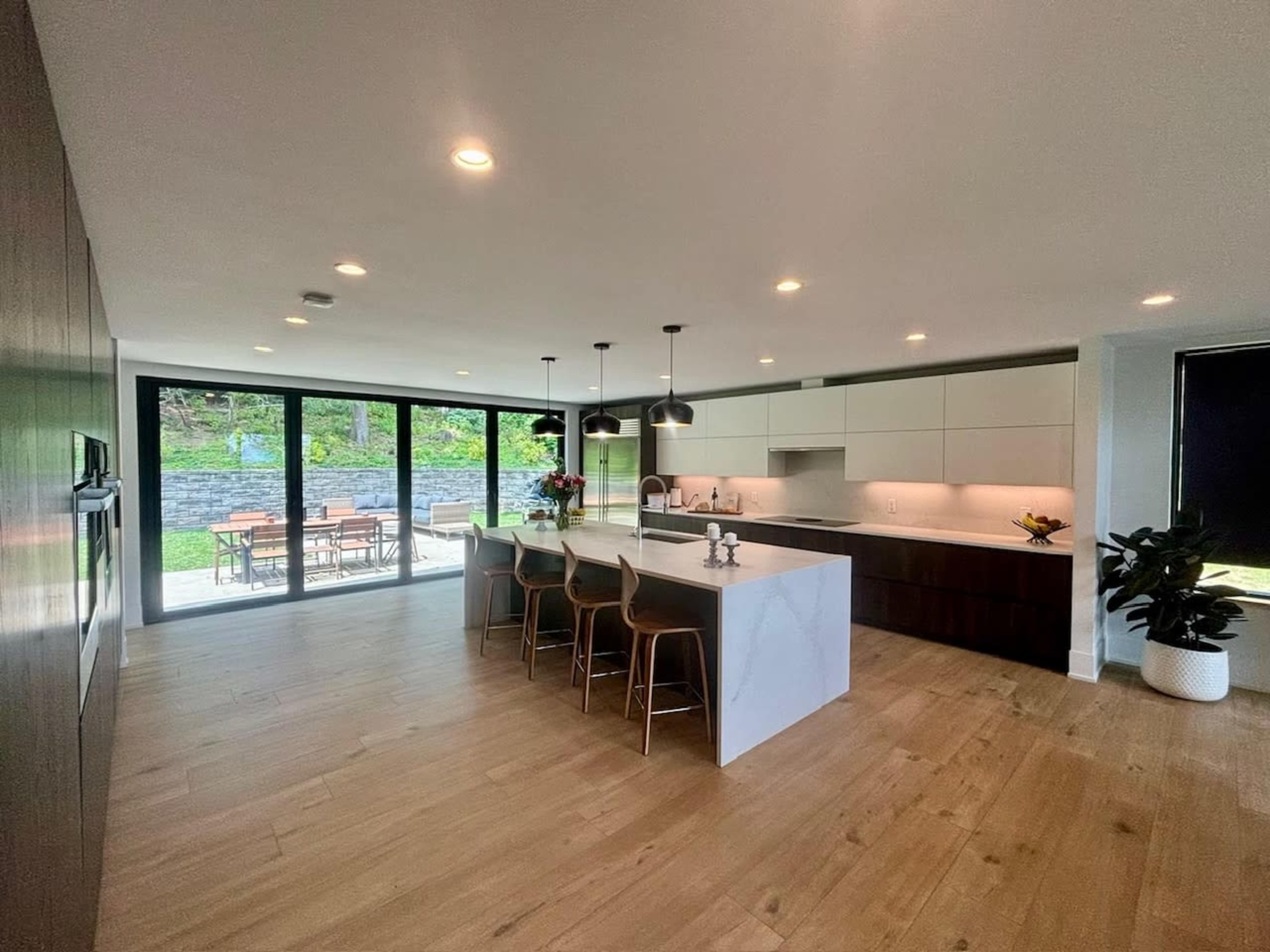 A modern kitchen with a large island and bar seating, featuring sleek cabinetry and large windows overlooking an outdoor seating area.