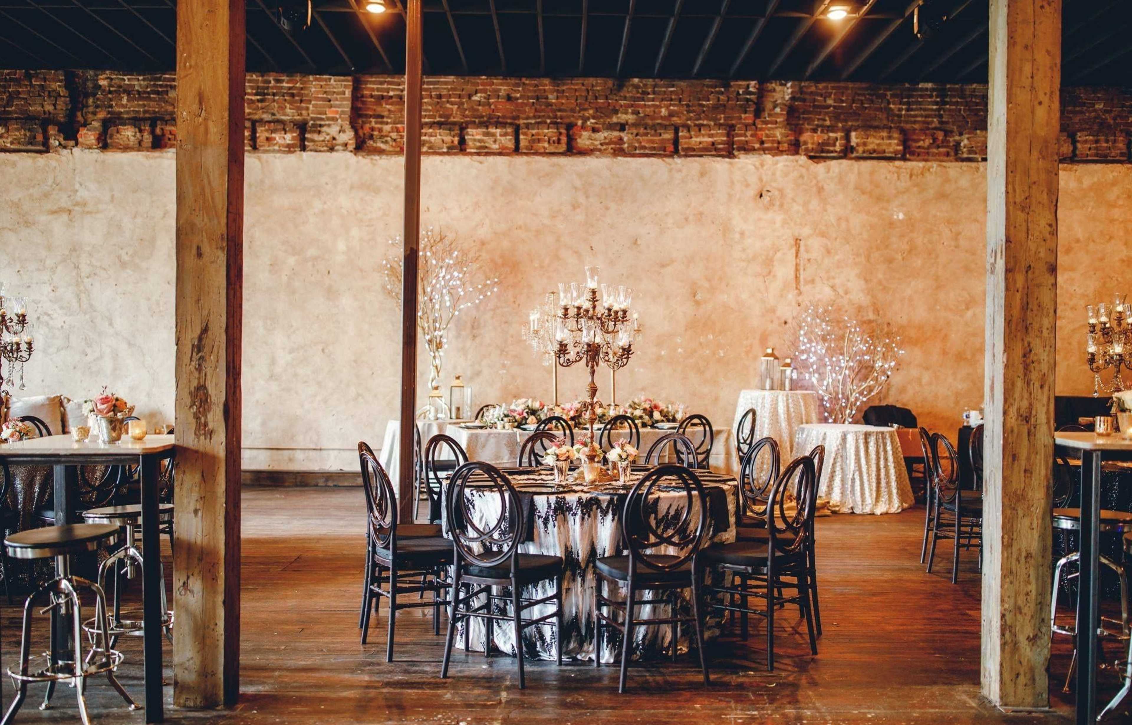 A spacious event venue with several decorated tables, candelabra centerpieces, and a mix of seating styles.