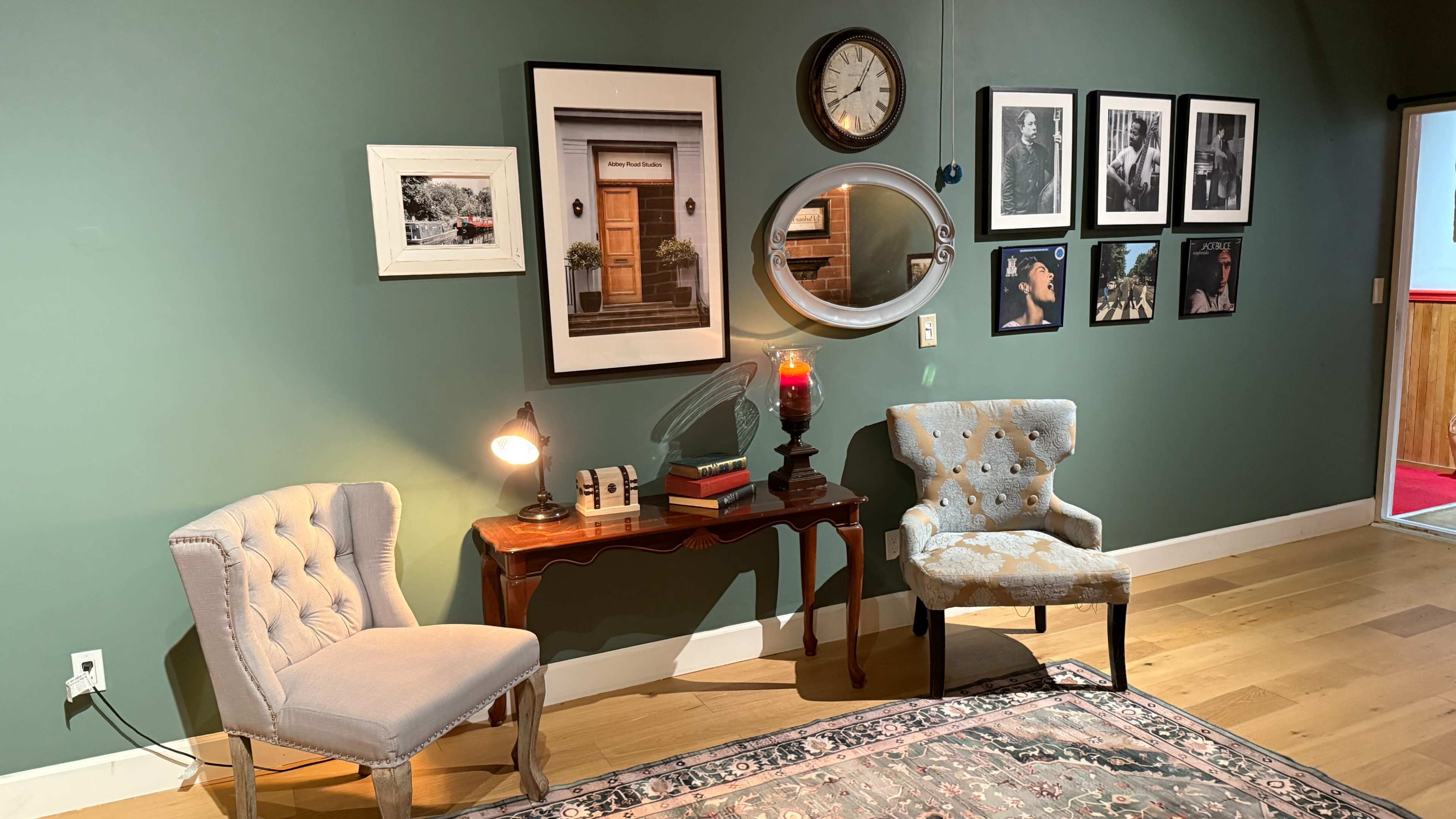The image shows a well-decorated corner of a room featuring two chairs, a side table with a lamp, and several framed photos on the walls.