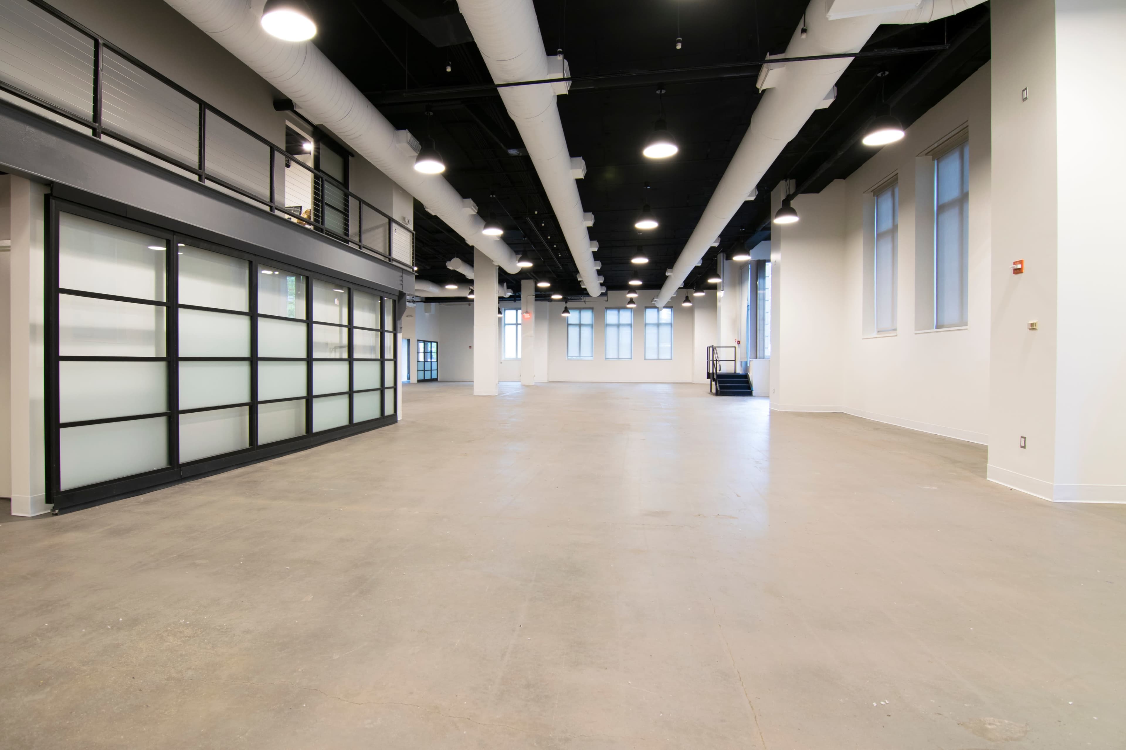 A spacious, empty interior of a commercial building with large windows and exposed ductwork on the ceiling.