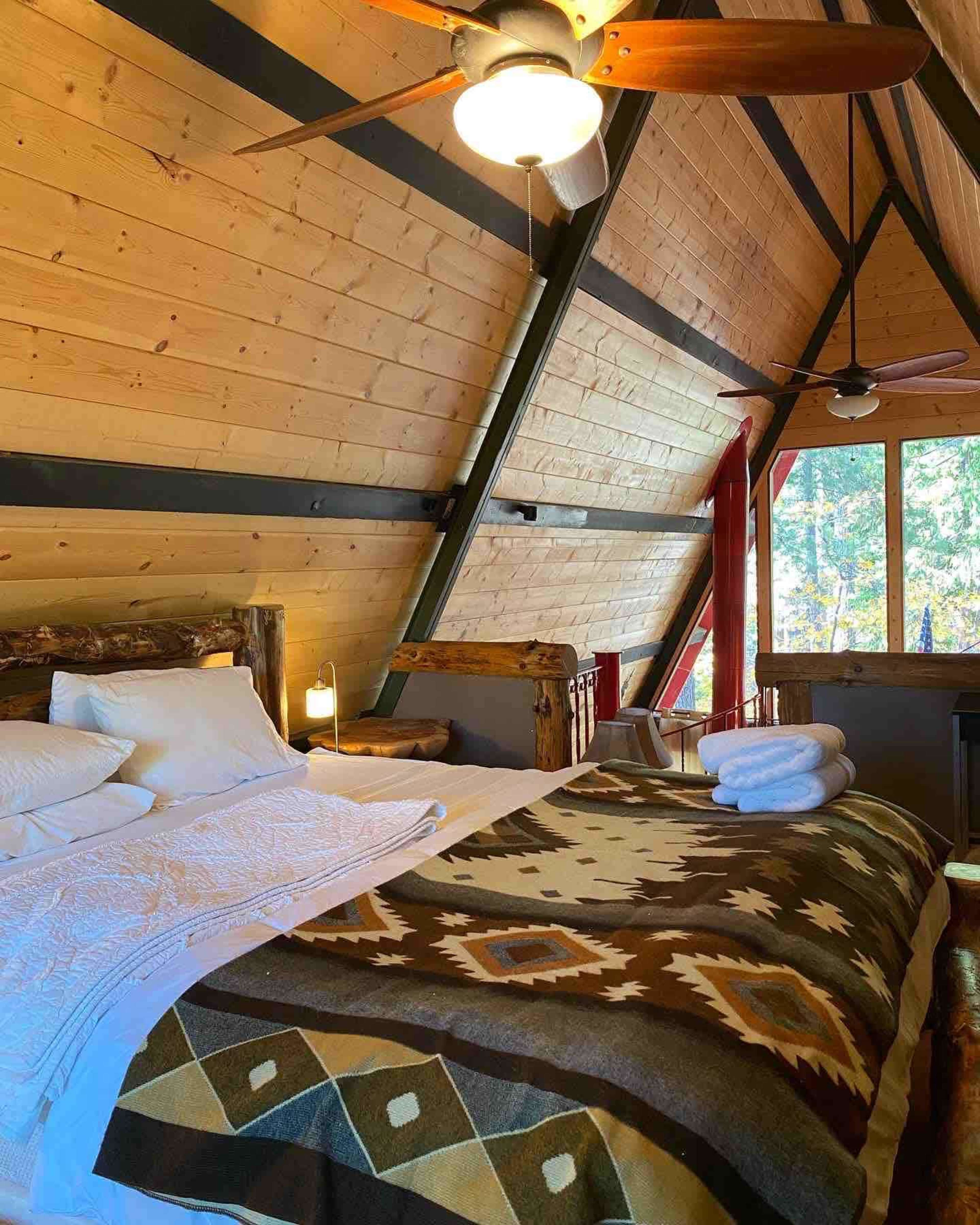 A cabin interior with an A-frame design, featuring a bed covered with a patterned blanket and two towels neatly arranged on a bedside table.