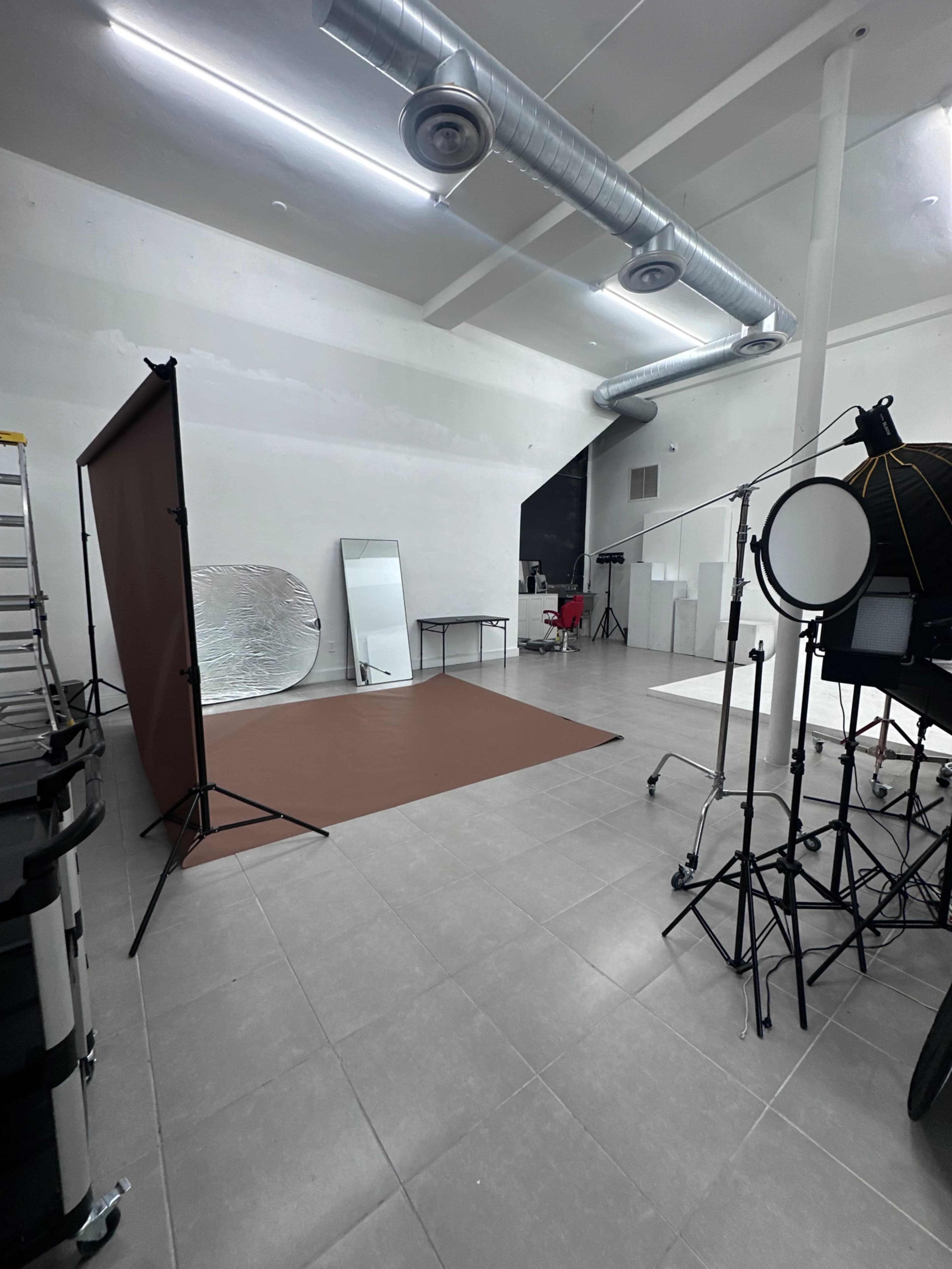 The image shows a photography studio with a brown backdrop, a mirror, and various equipment including lighting stands and a chair.
