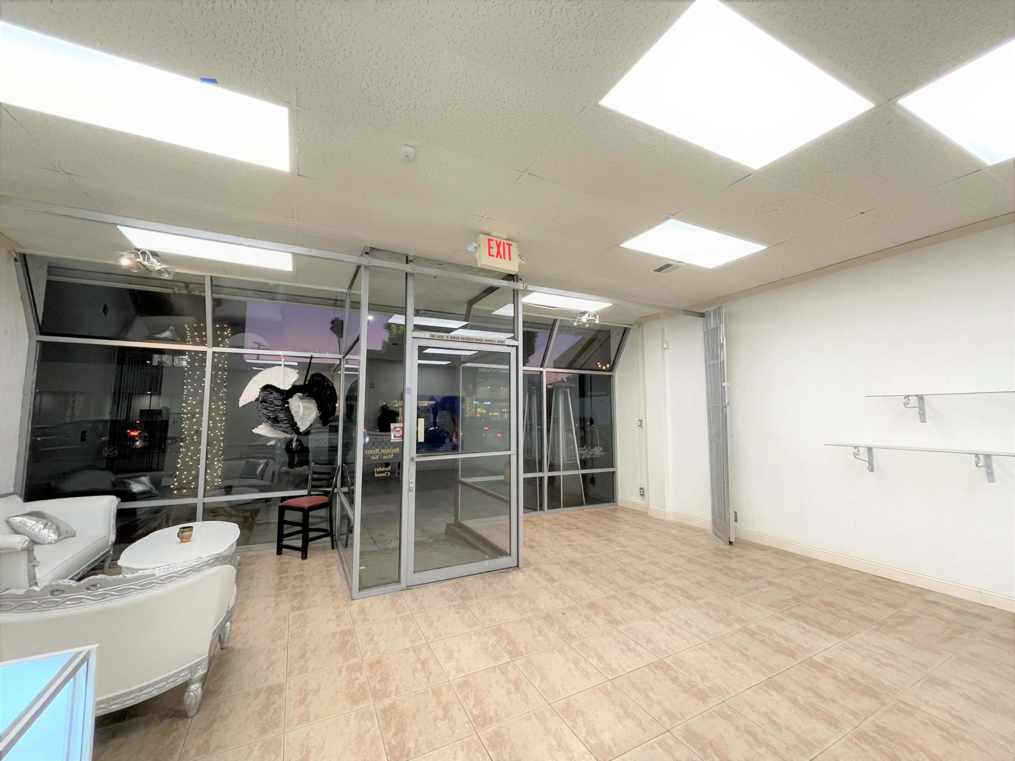 An empty retail space with glass doors, a decorative white sofa, and beige tiled flooring.