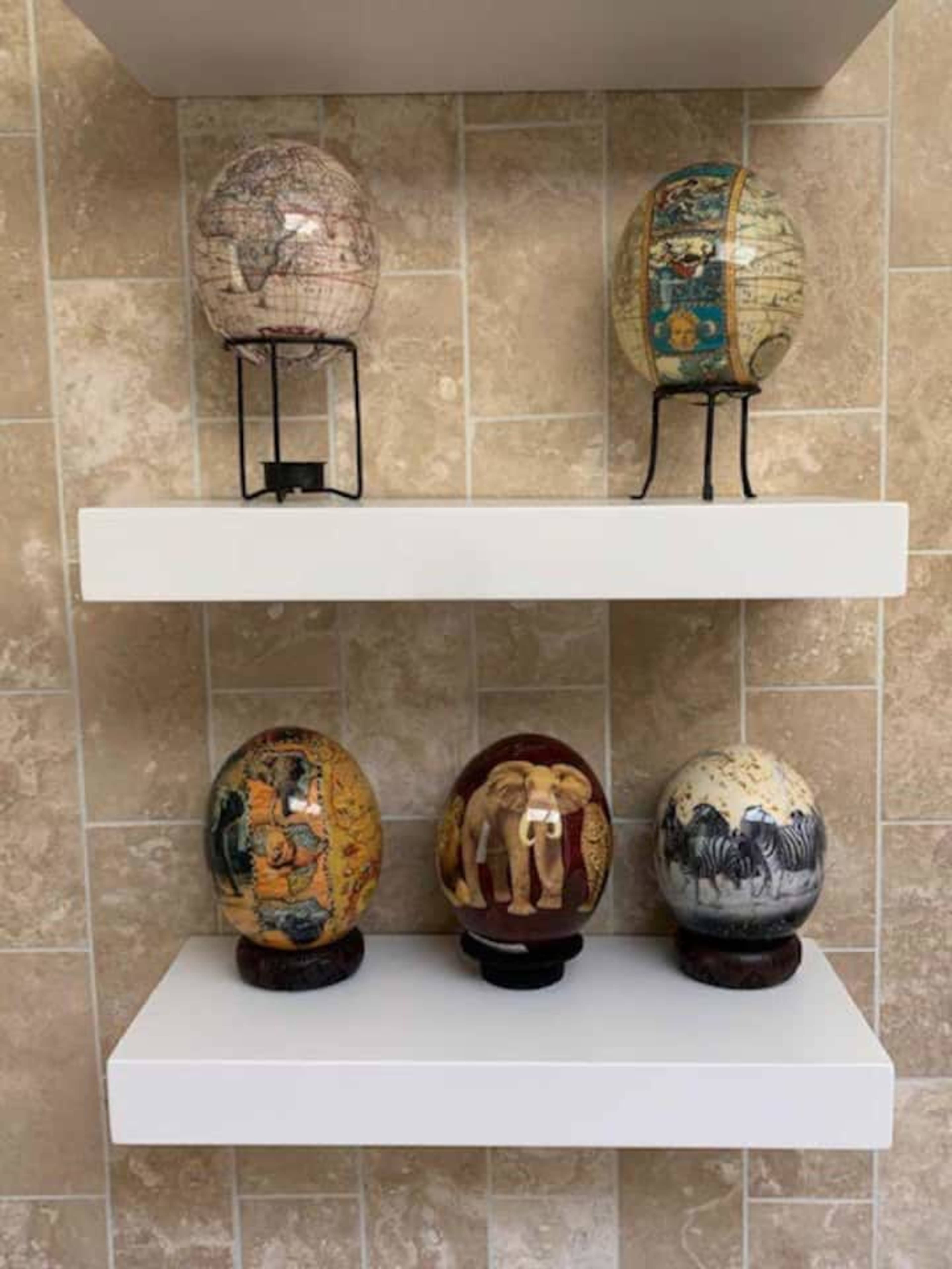The image shows decorative globes and painted eggs arranged on two white shelves against a tiled wall.