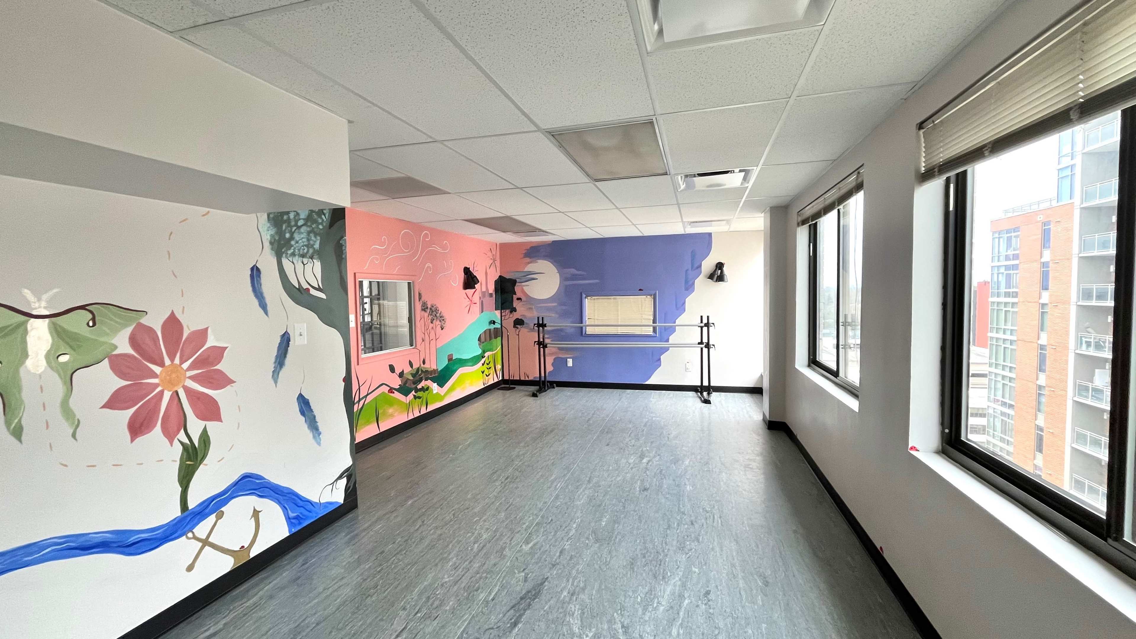 A spacious room with murals on two walls featuring a large flower, flowing water, and abstract designs, along with large windows letting in natural light.