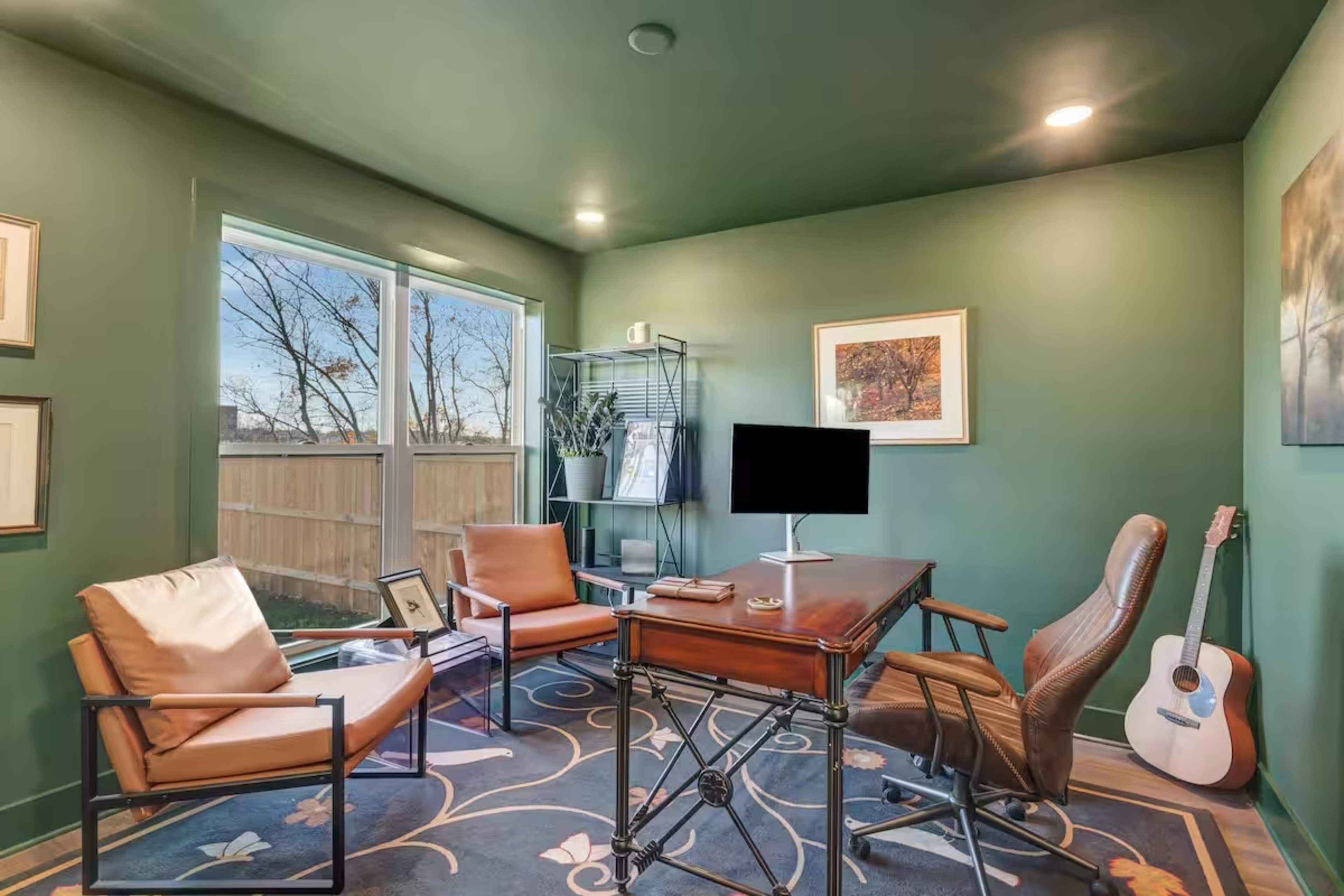 The image features a cozy office space with green walls, a wooden desk, two leather chairs, and a guitar resting against the wall.