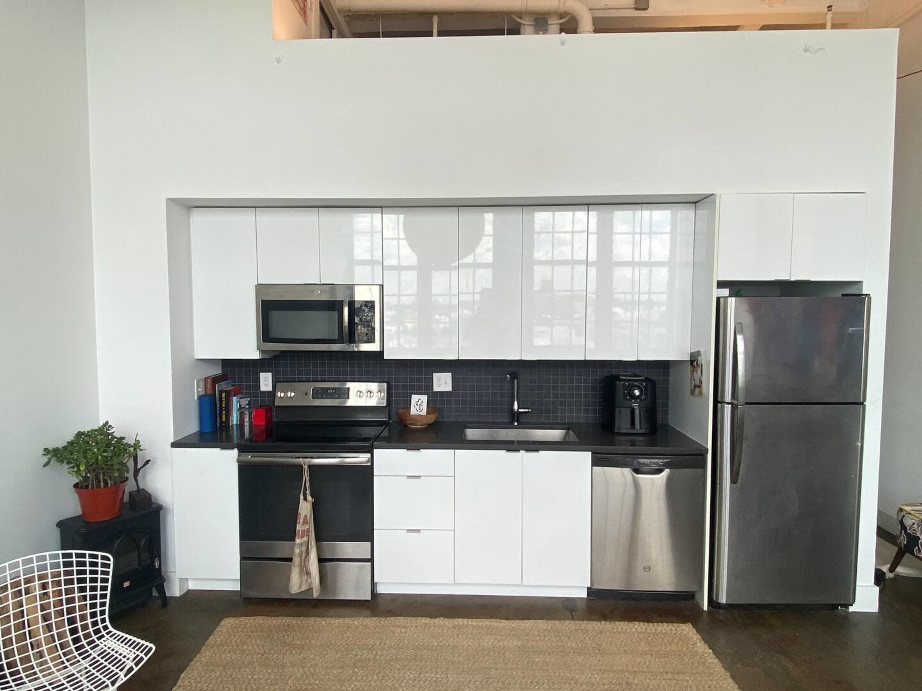 A modern kitchen with white cabinetry, stainless steel appliances, a black countertop, and a small plant on the counter.