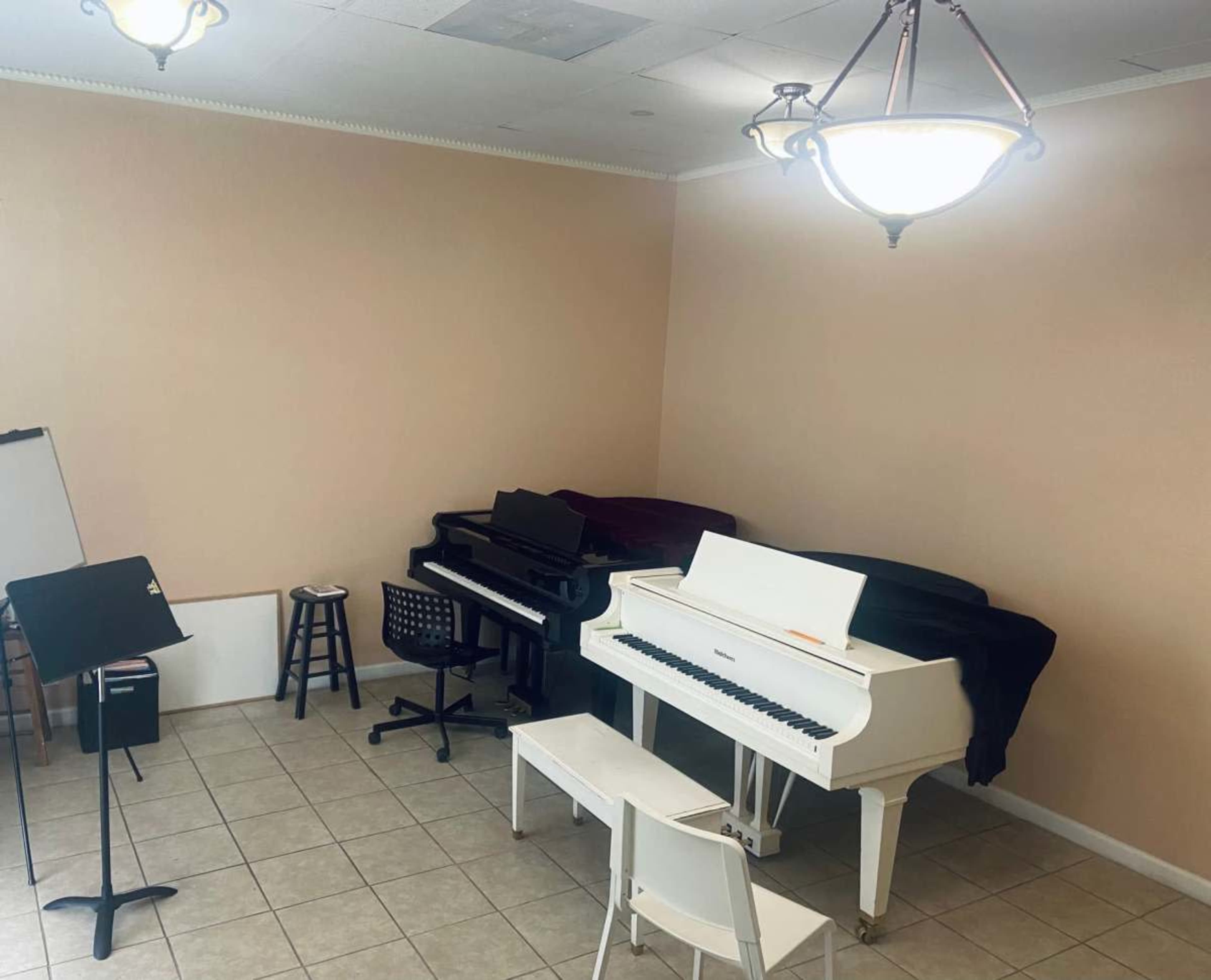 The room contains two pianos, one white and one black, along with a music stand and a stool.