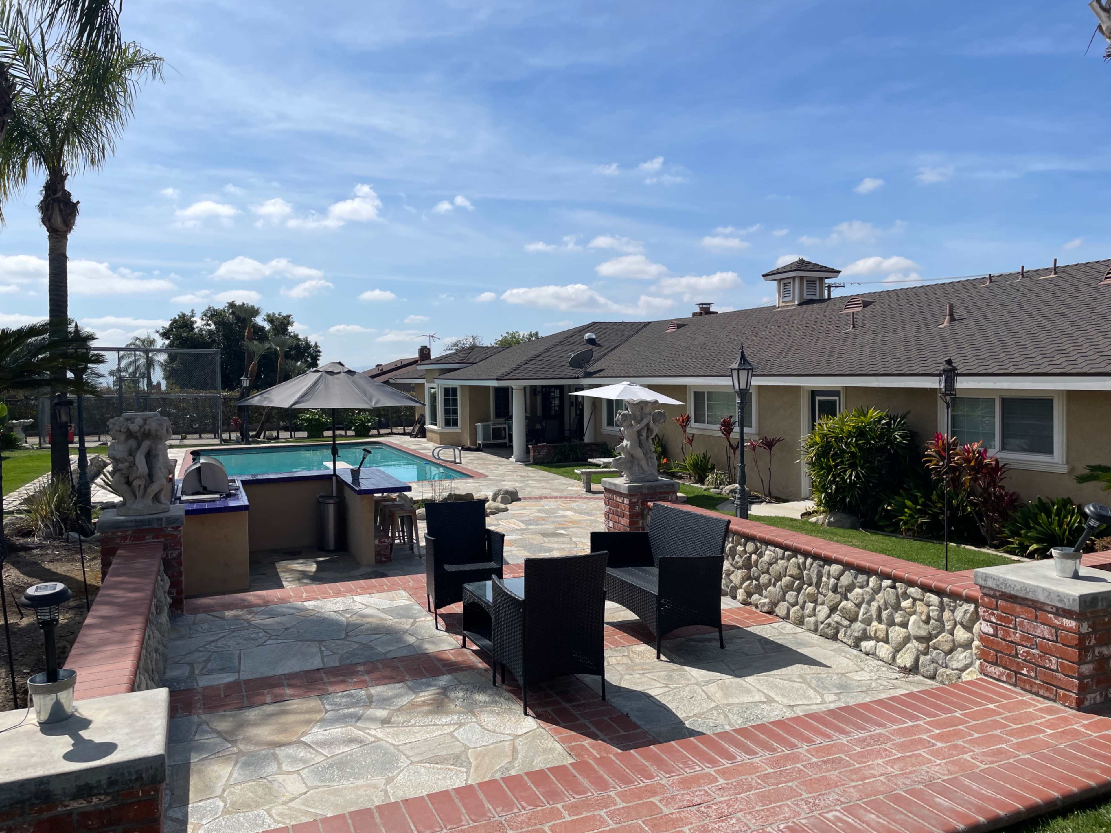 A landscaped backyard features a swimming pool, patio furniture, and a house with a tiled roof.