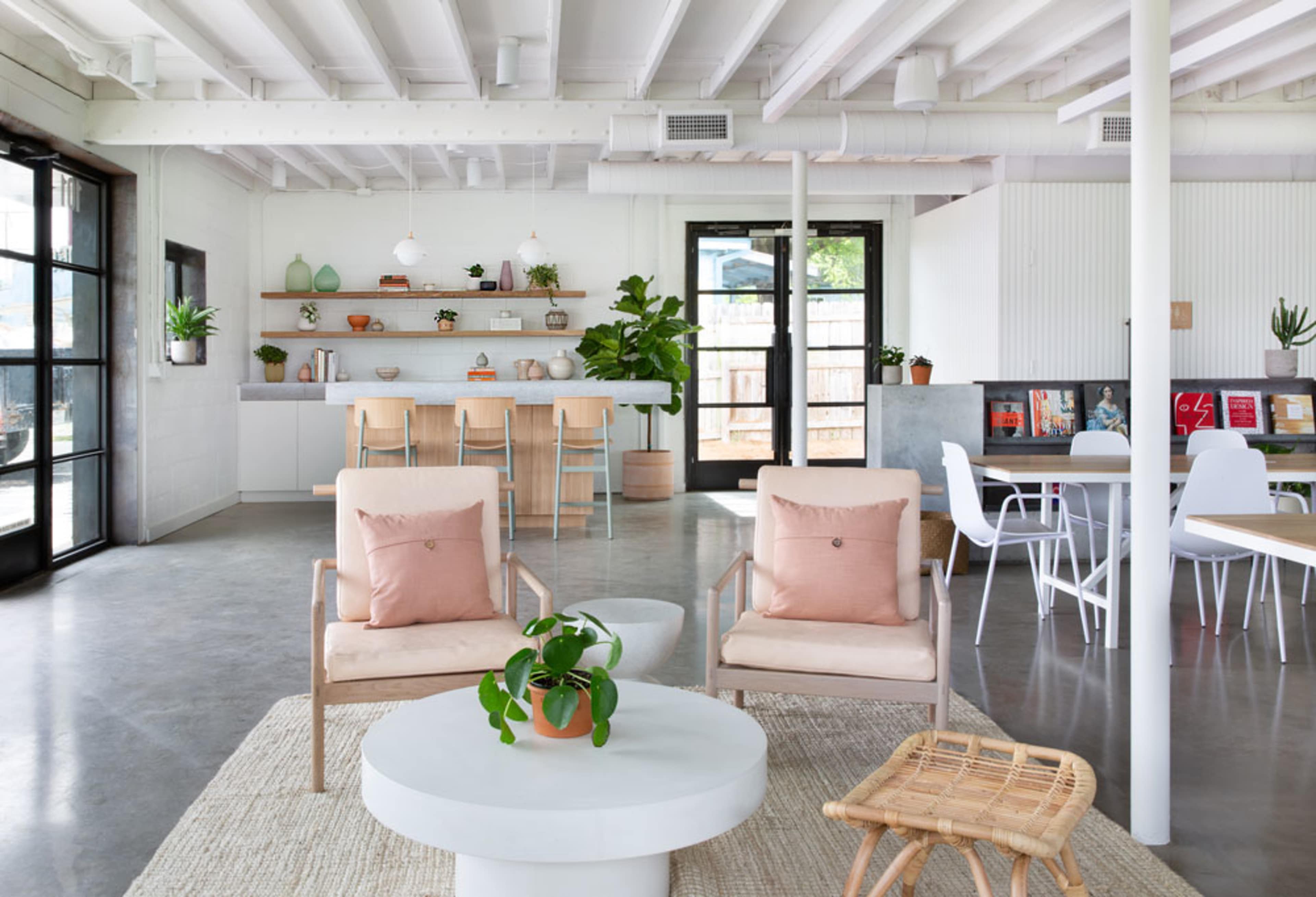 The image shows a modern open-plan interior with a seating area featuring two armchairs, a round coffee table, and a kitchen counter in the background.