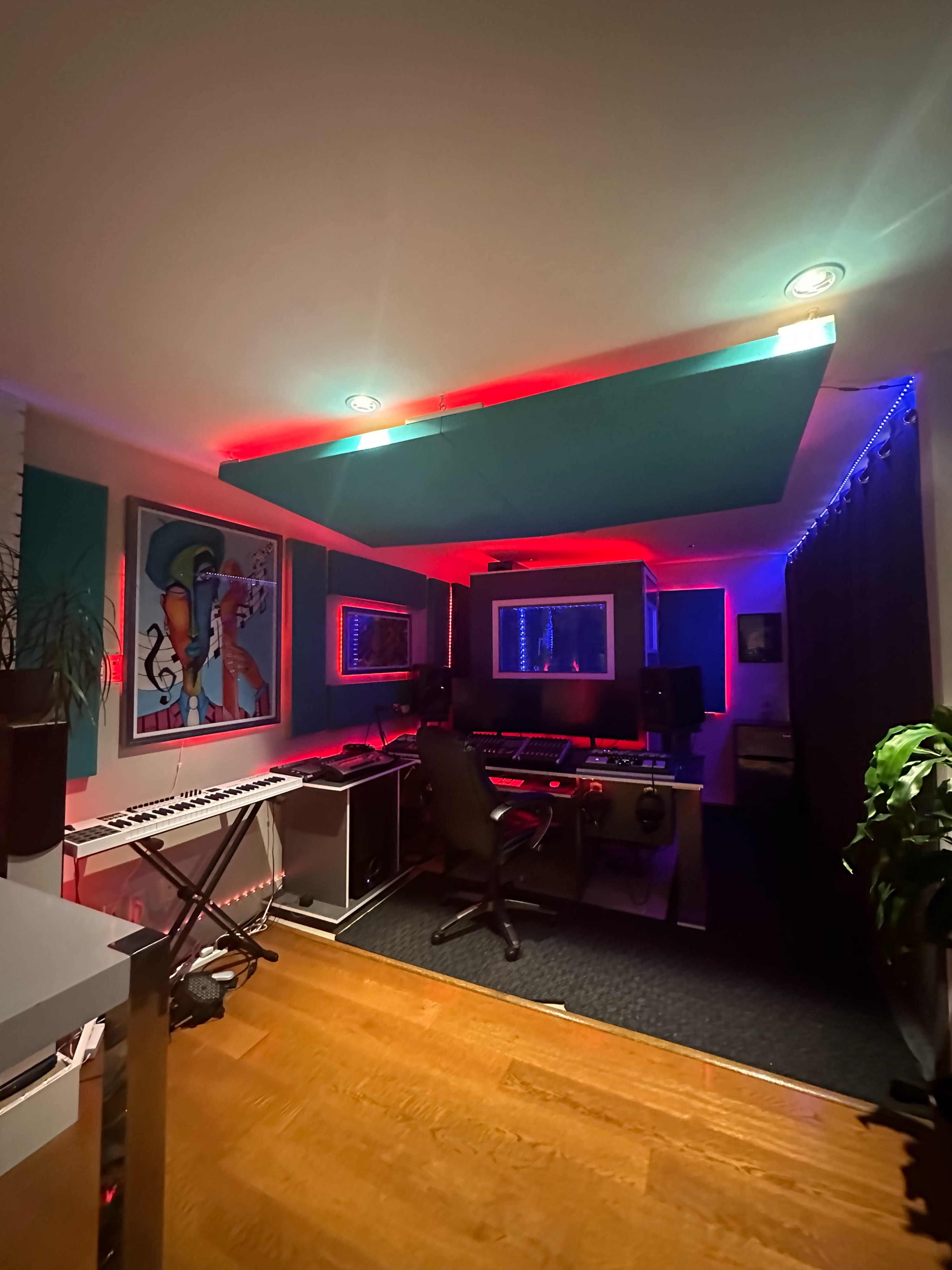 A modern music production studio with colorful LED lighting, a computer setup, and musical instruments.