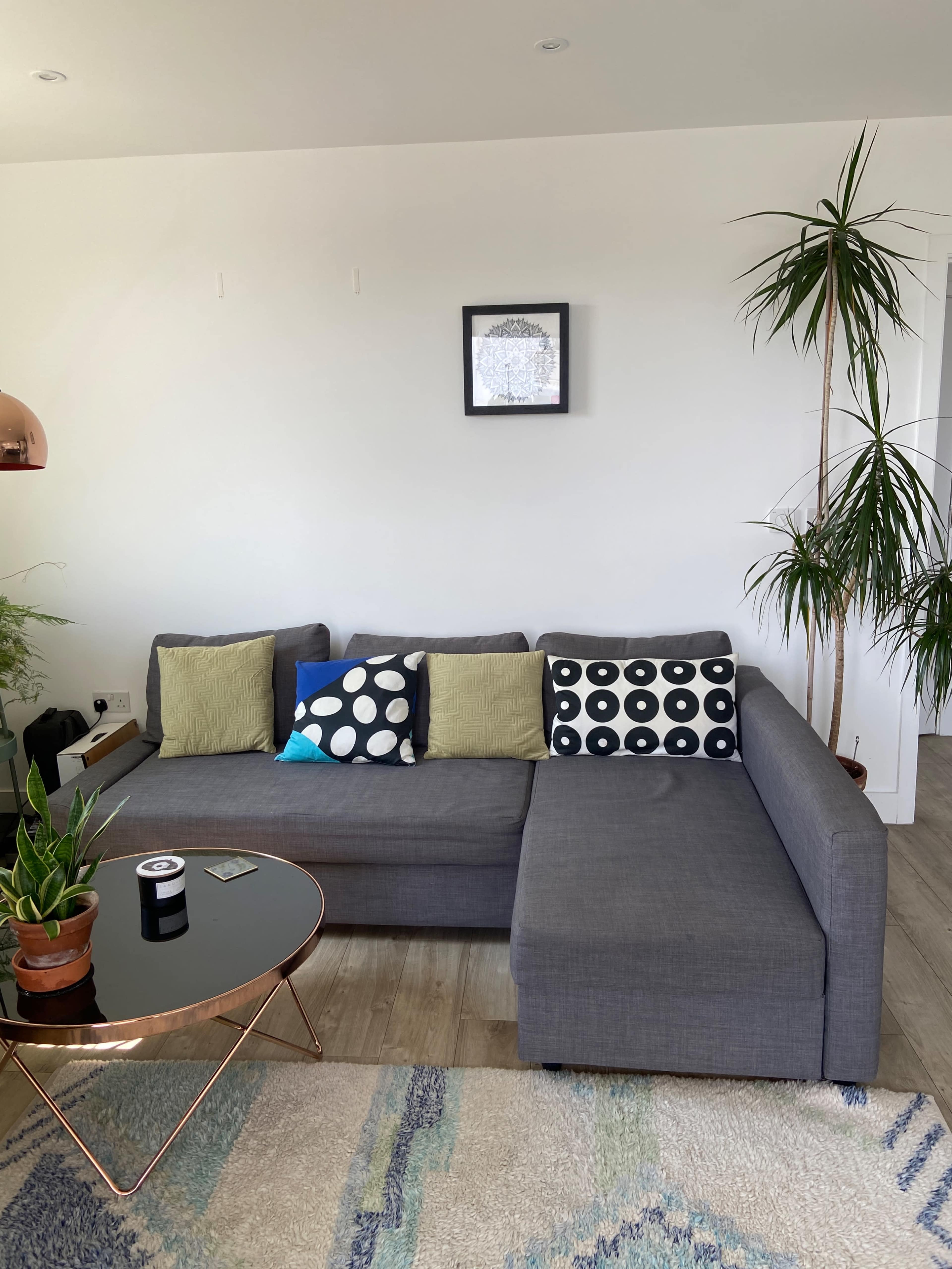 A modern living room features a gray sectional sofa with decorative cushions, a round coffee table, and a tall plant in a pot.