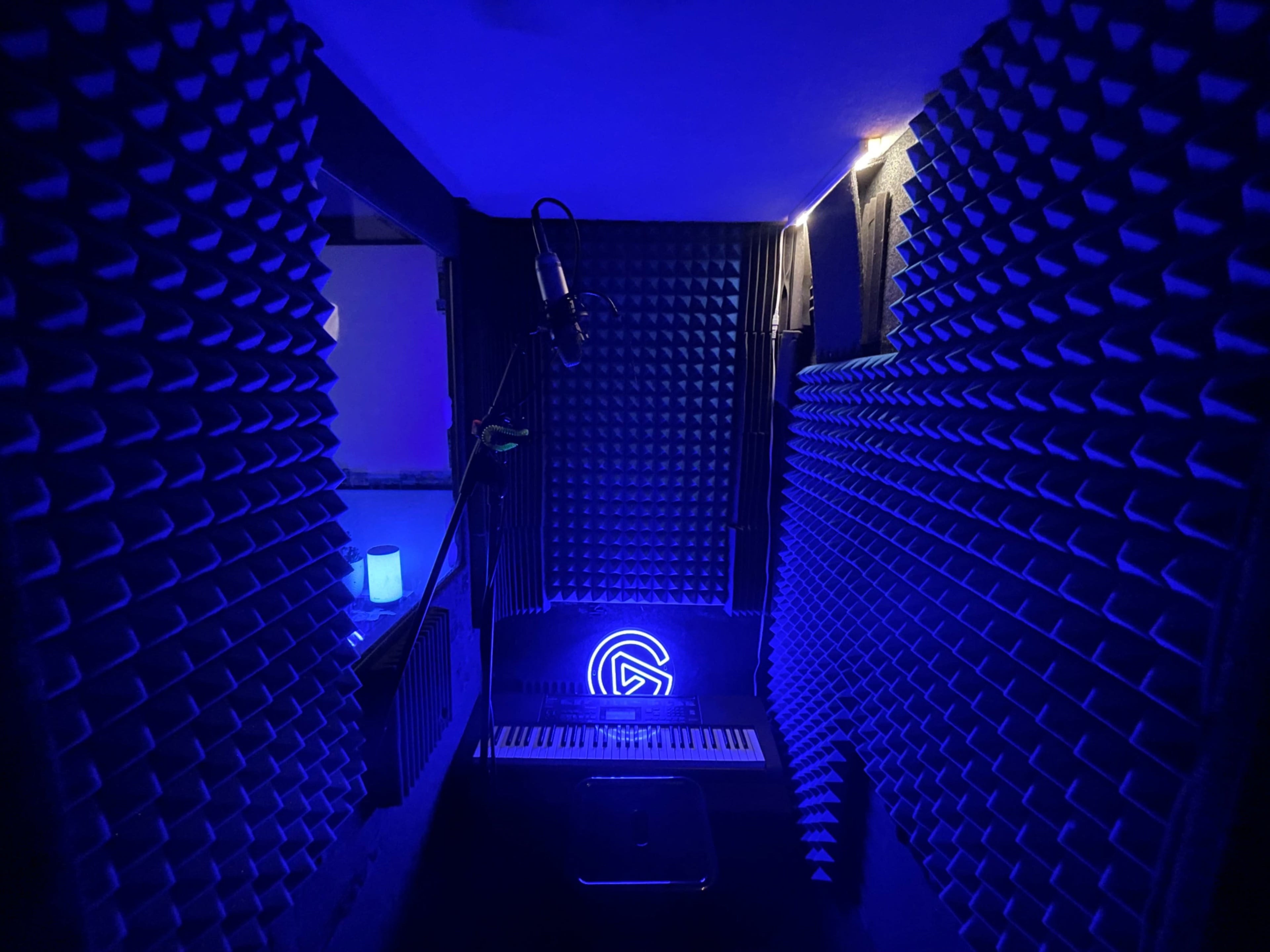 A soundproof recording studio with foam sound panels, a microphone on a stand, and blue ambient lighting.