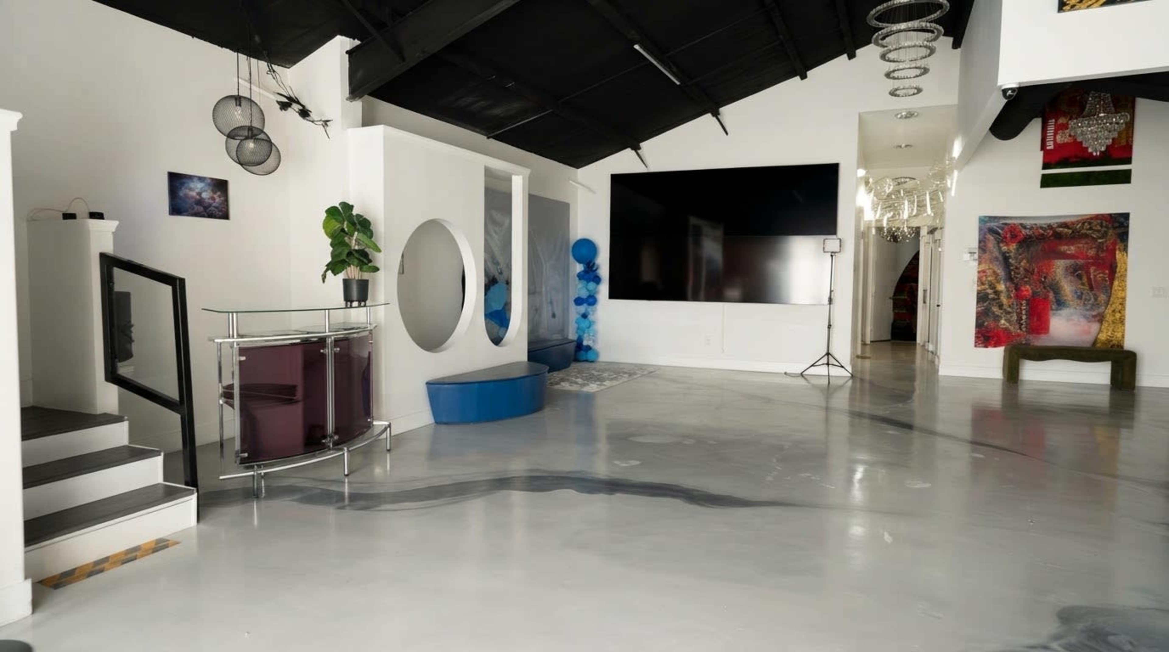 The image shows a modern, spacious interior with a polished concrete floor, large wall-mounted television, and decorative elements like artwork and plants.