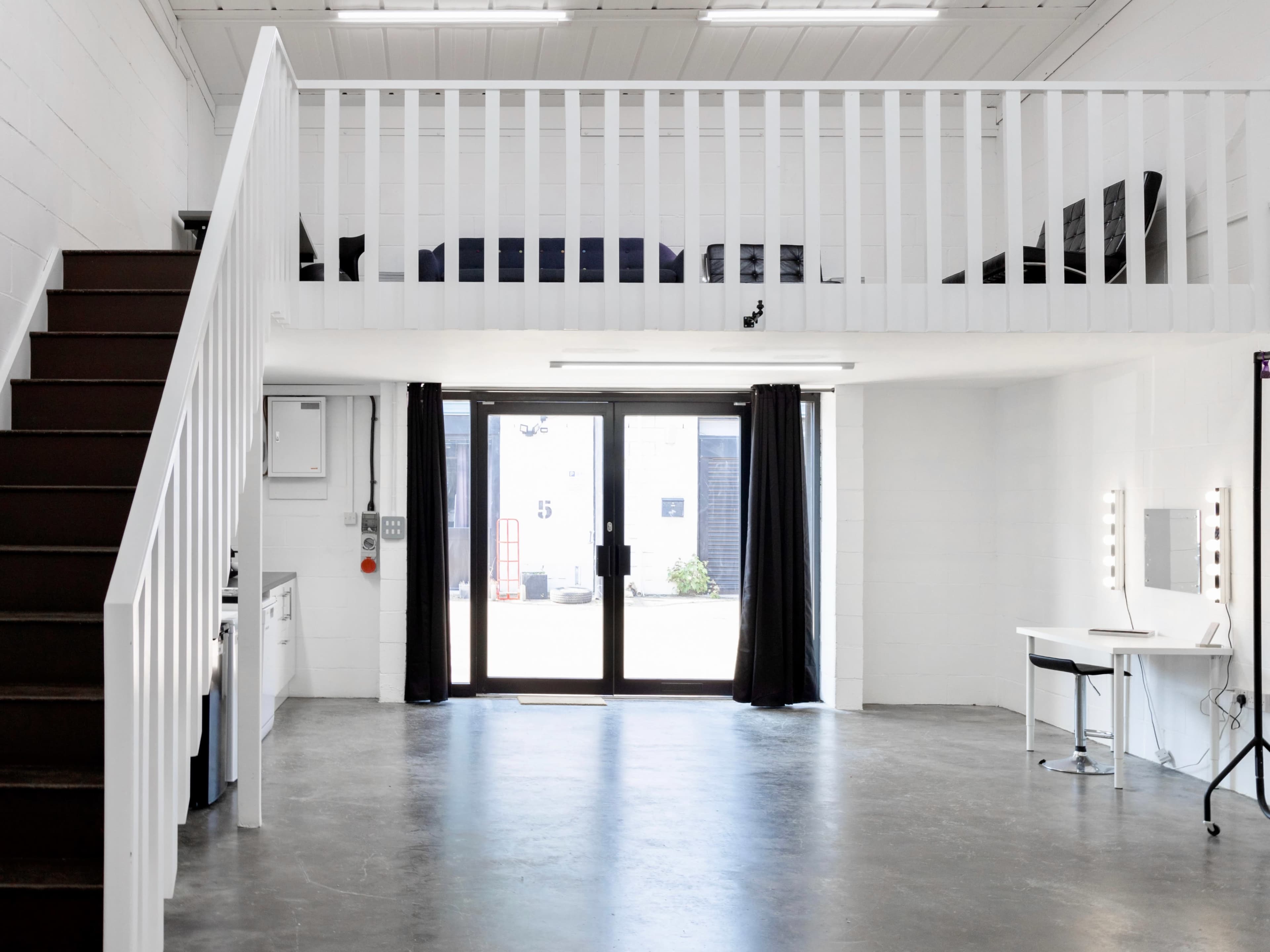 An interior space with a staircase leading to a loft area, featuring a large glass door and a vanity table with lights.