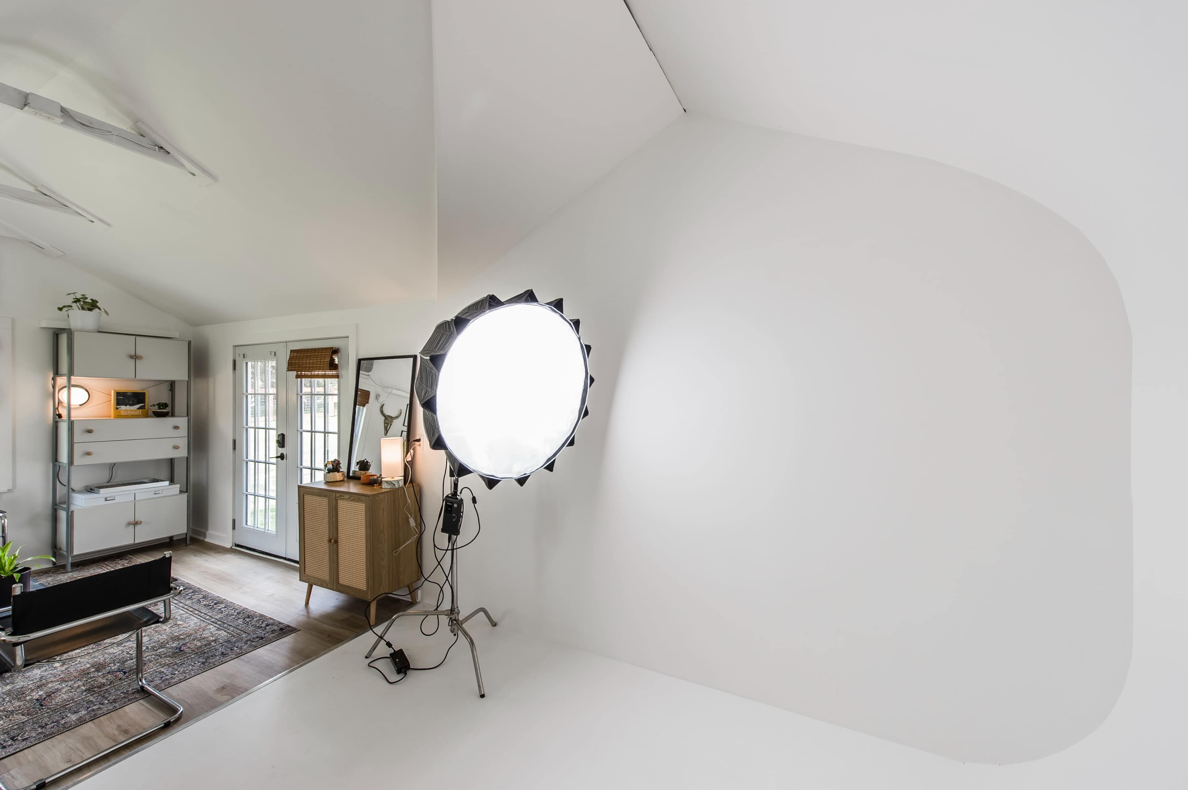 The image shows a bright, minimalistic studio space featuring a circular softbox light and a neutral-colored wall.