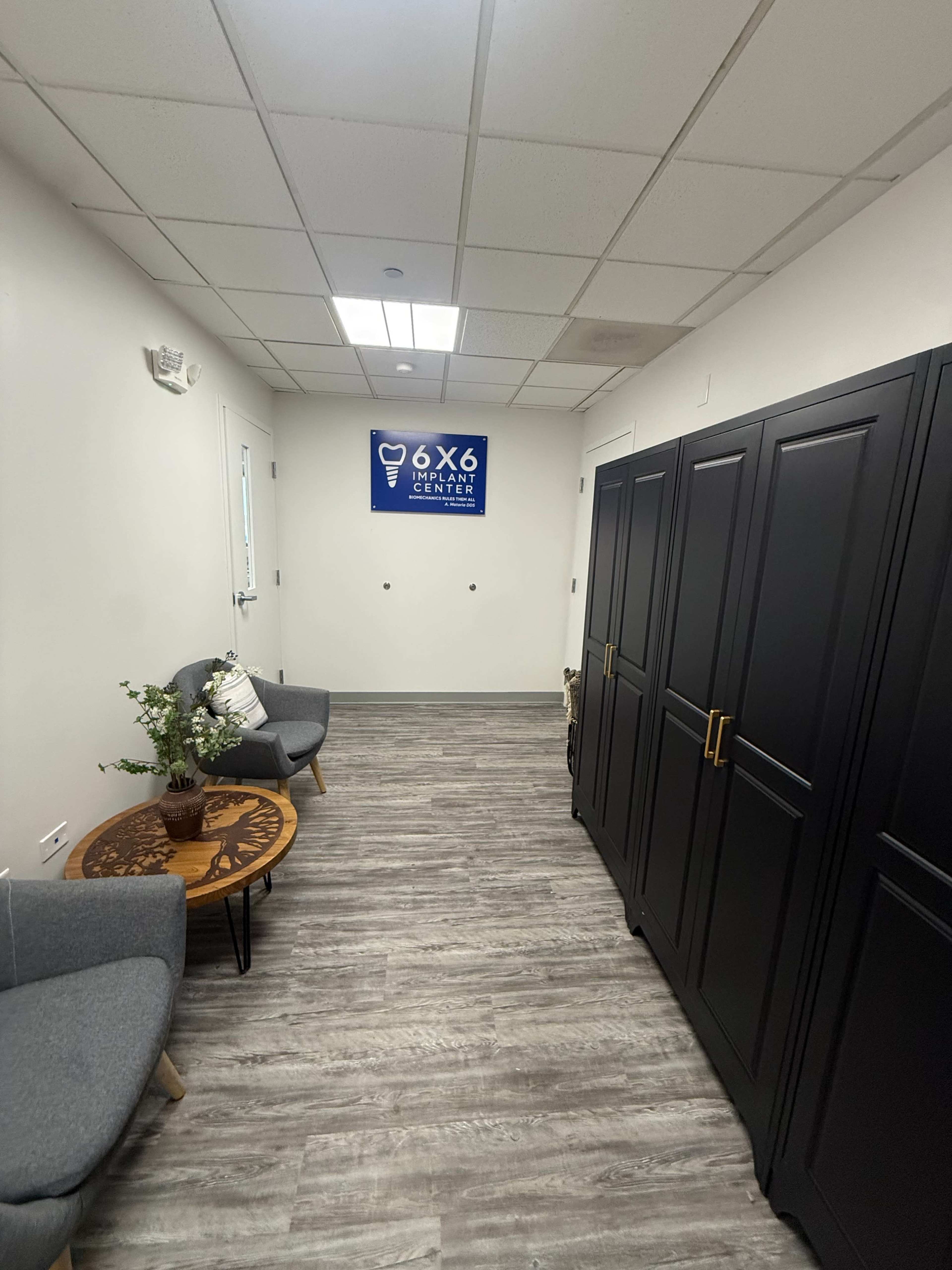 The image shows a narrow hallway with a sign for "6x6 Jensen," two gray armchairs, a small round table with a plant, and a row of black lockers along one wall.