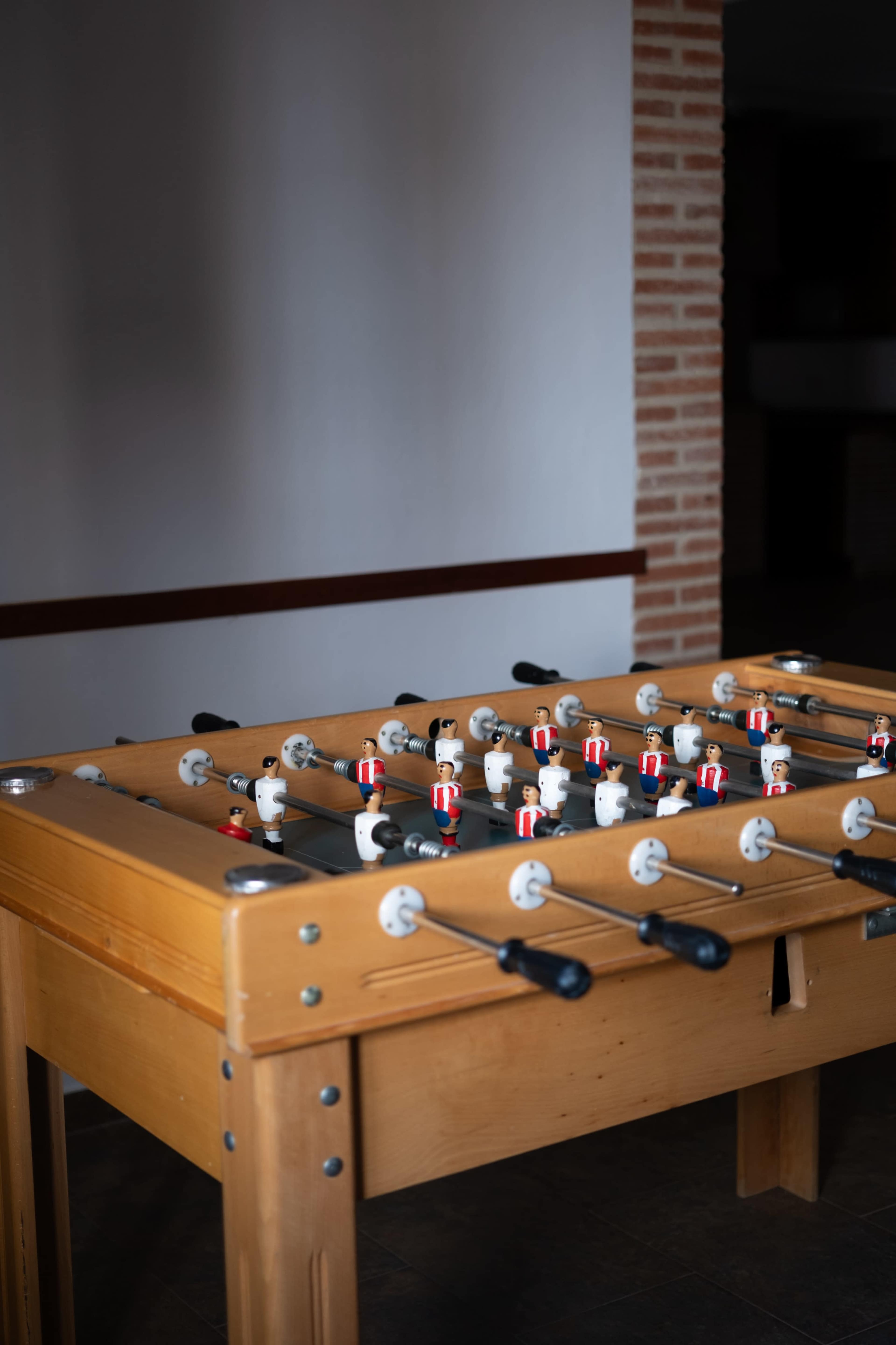 A wooden foosball table with players positioned on rods is set against a plain wall.