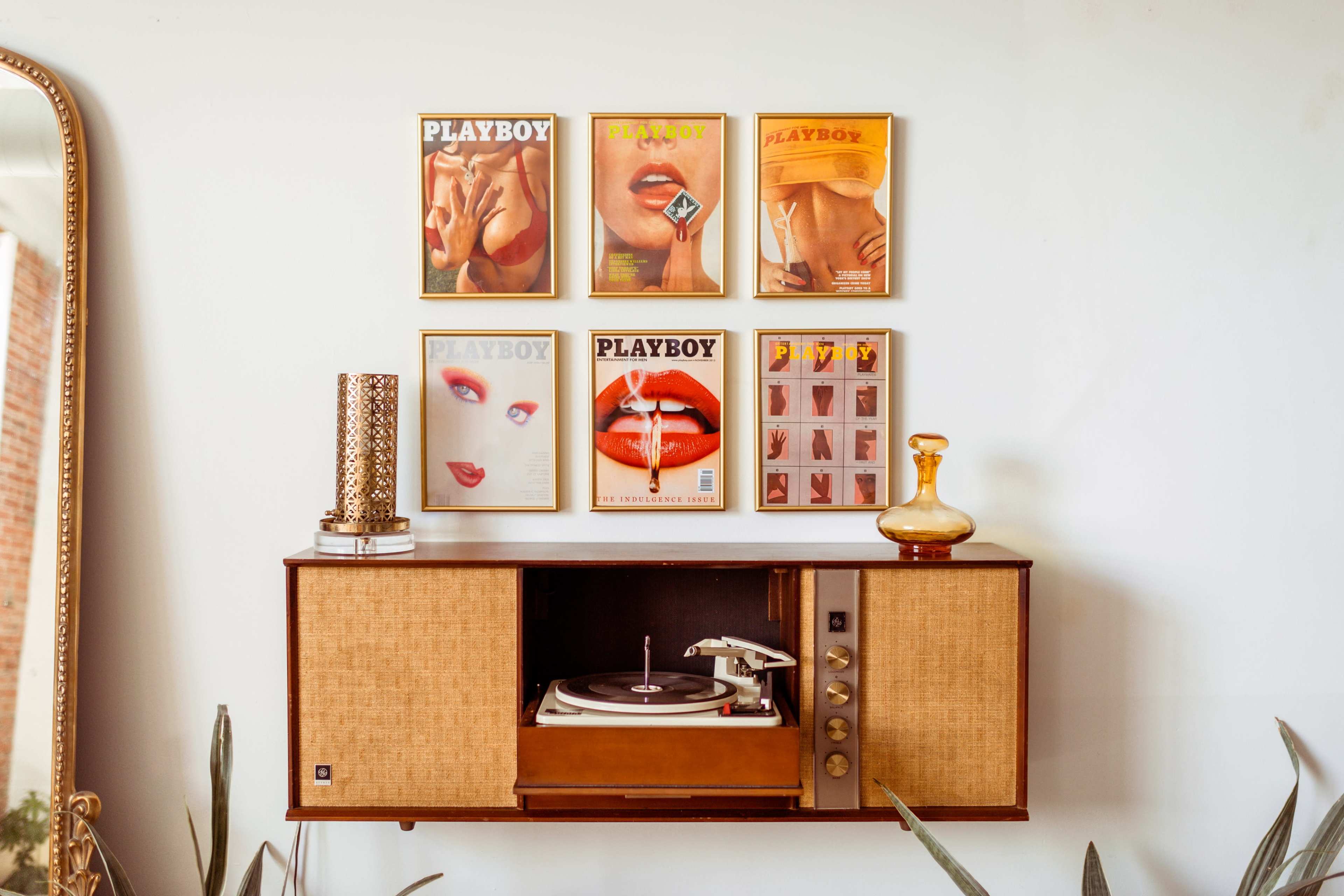 A vintage record player stands beneath a wall displaying framed Playboy magazine covers.