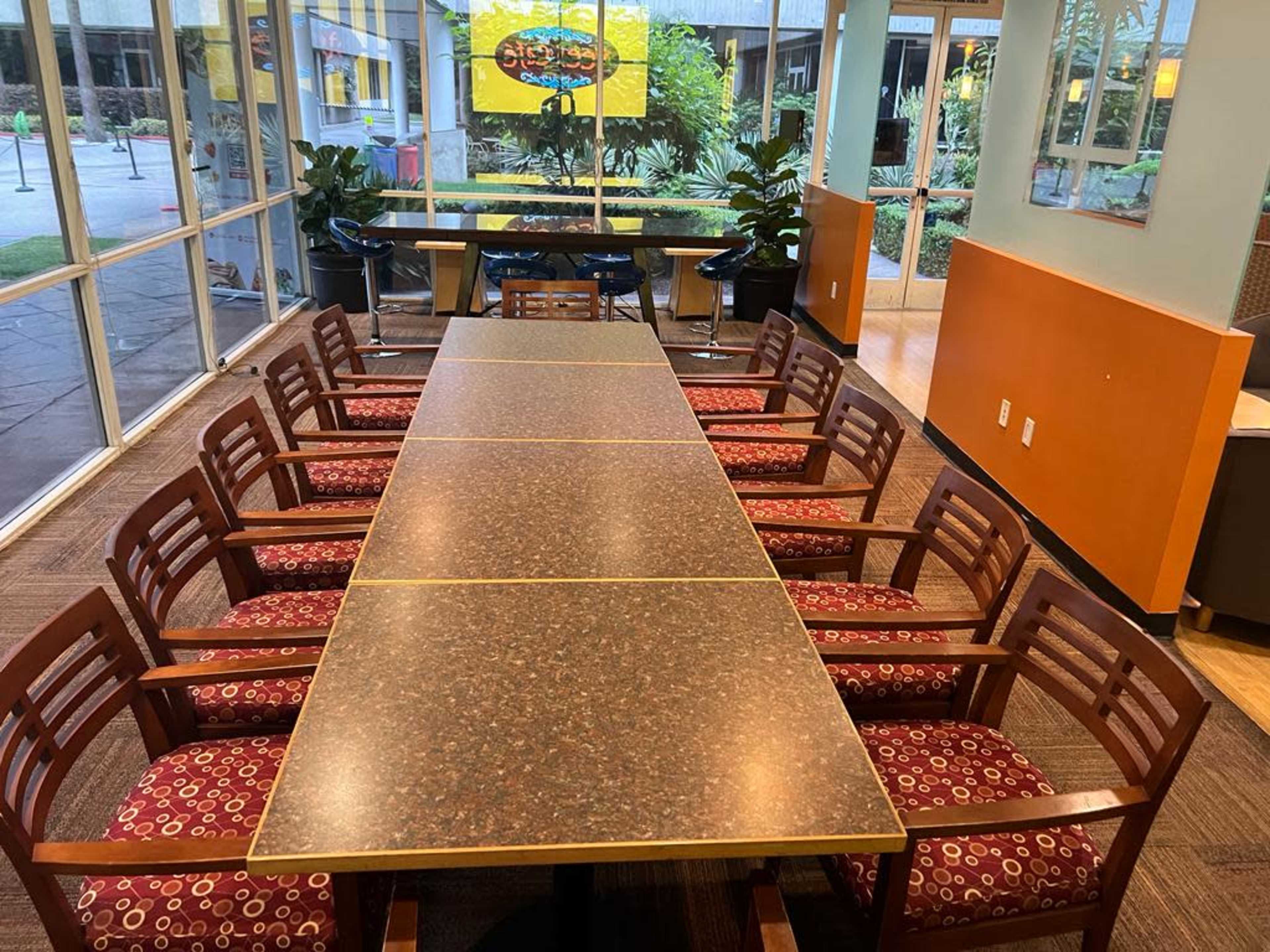 A long, rectangular table with wooden chairs lined on both sides in a well-lit indoor setting.