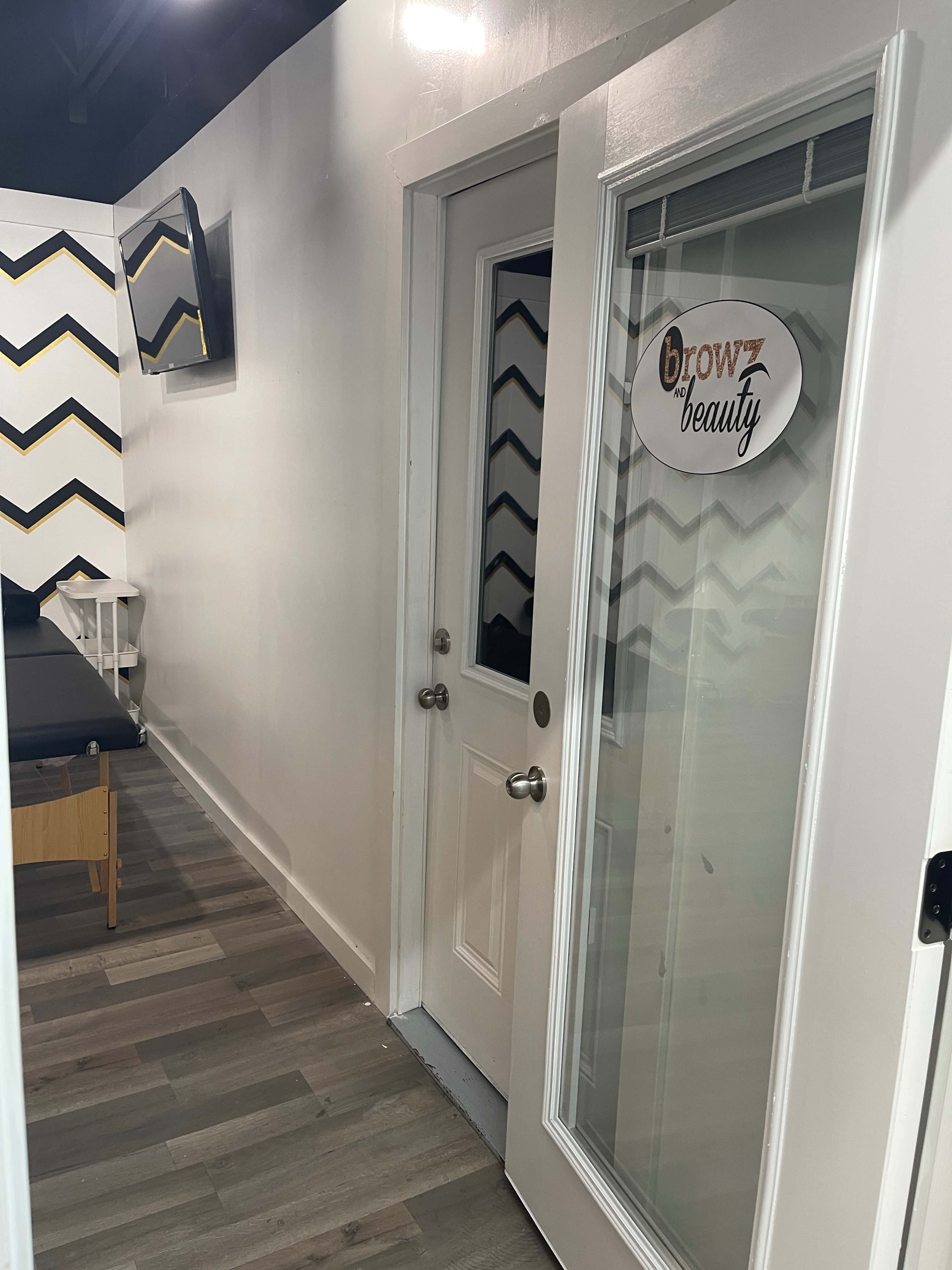 A well-lit salon hallway leading to a door labeled "brow beauty," with a zigzag patterned wall in the background.