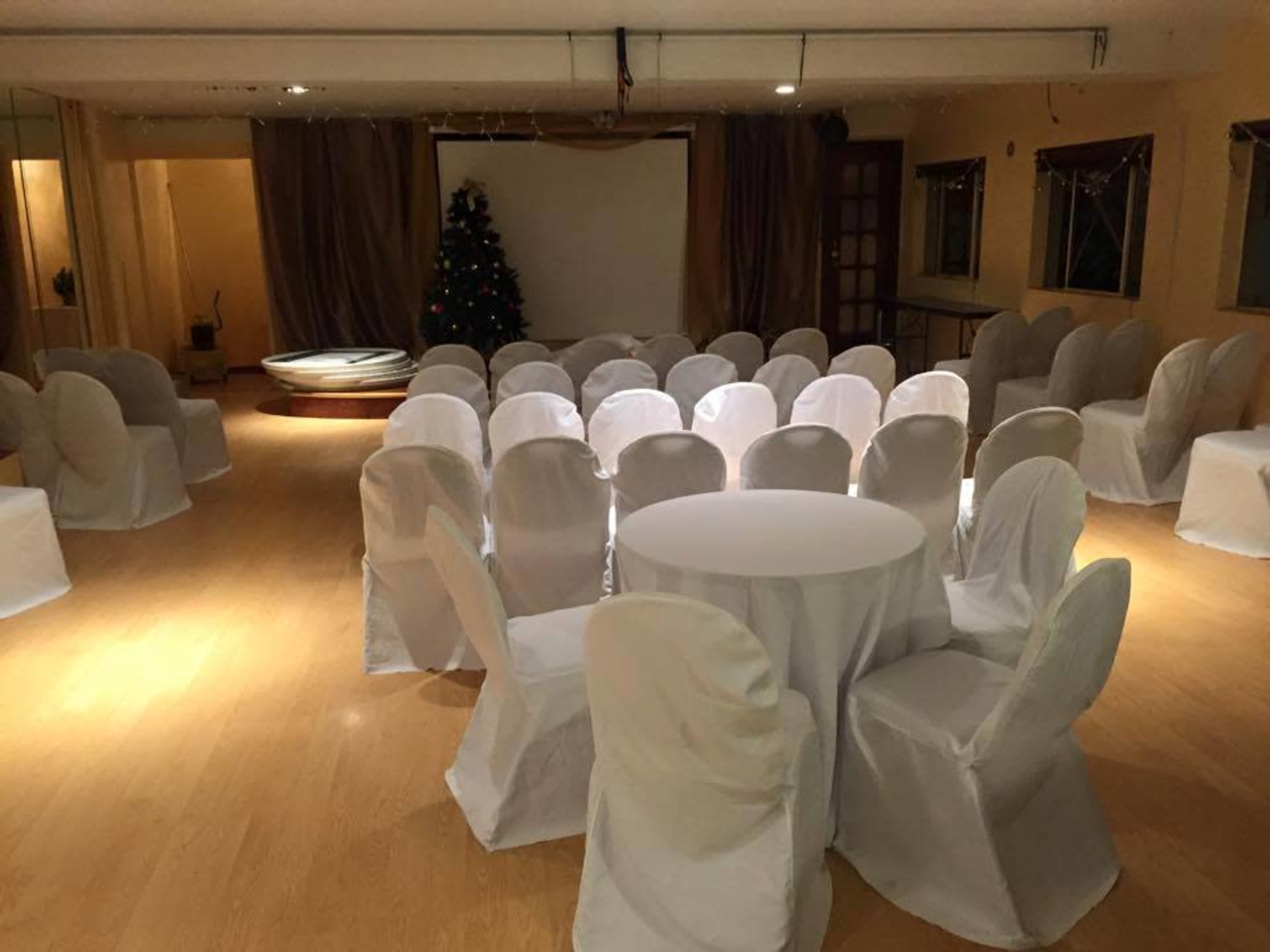 The image shows a spacious event room set up with rows of covered chairs facing a blank screen, with a decorated Christmas tree in the corner.