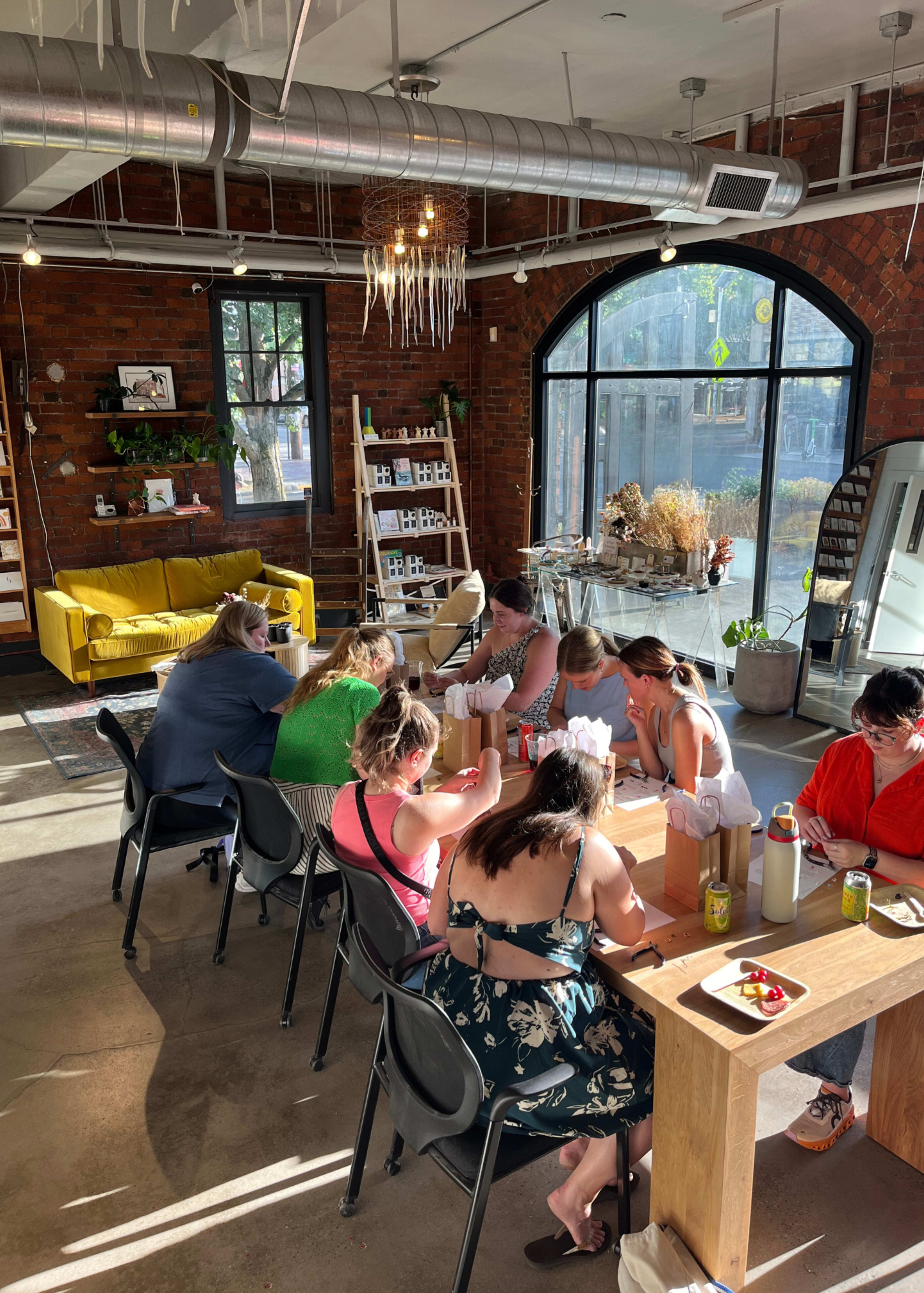 A group of people is seated around a long table in a bright, modern space with large windows and exposed brick walls.