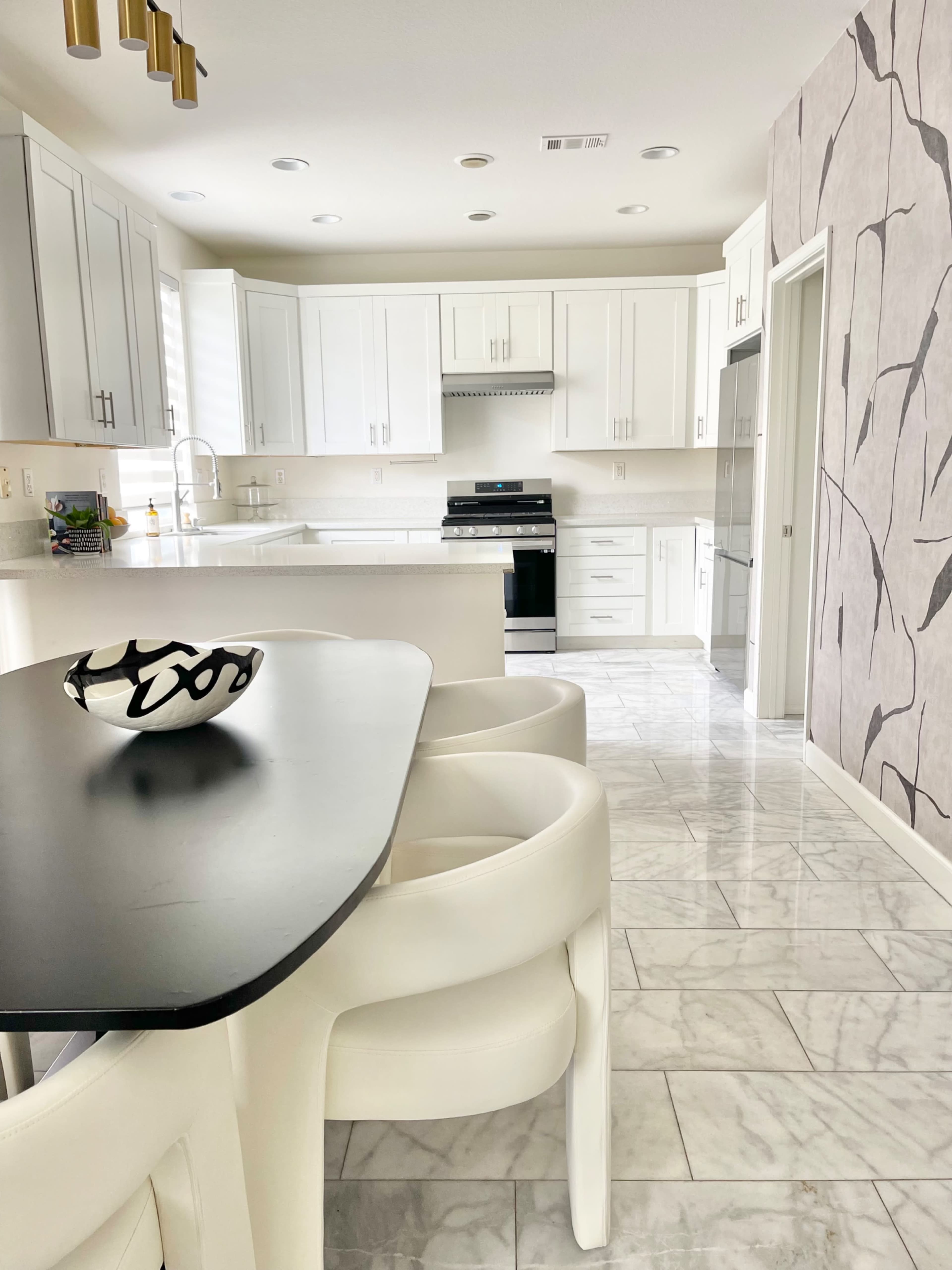 A modern kitchen features white cabinetry, a marble floor, and a black dining table with white chairs.