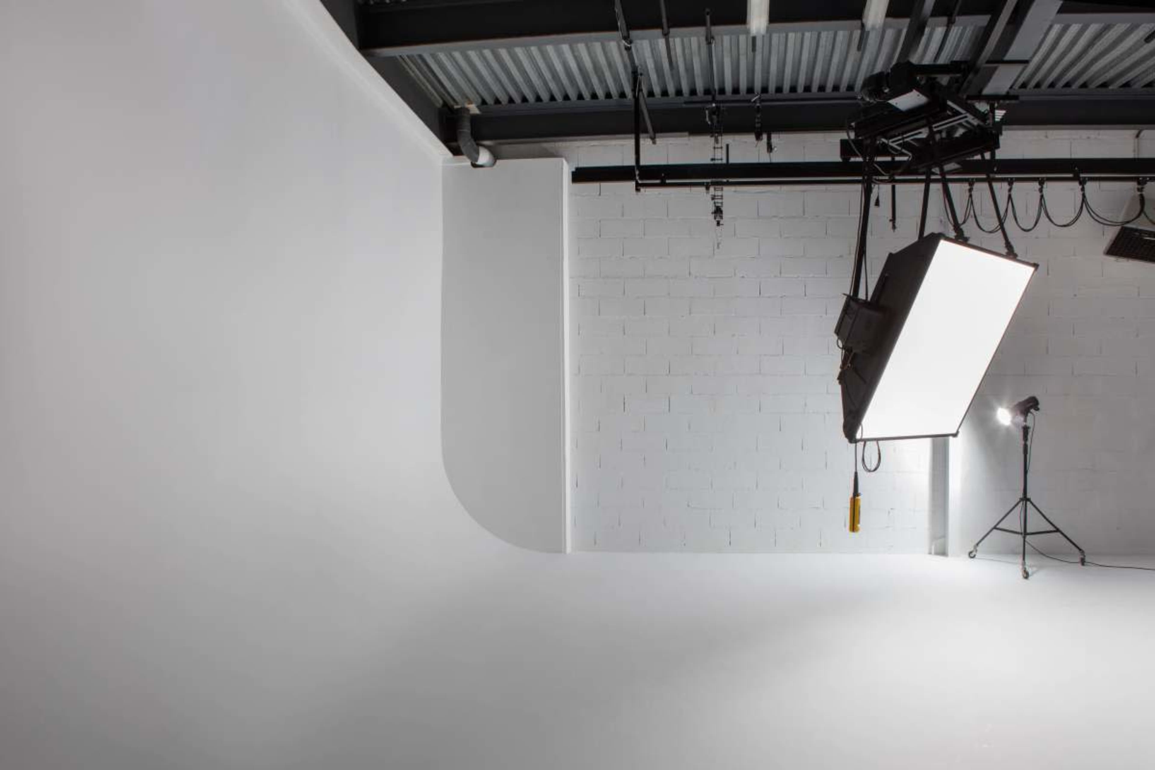 The image depicts a spacious, empty photography studio with white walls and a large softbox light hanging from the ceiling.