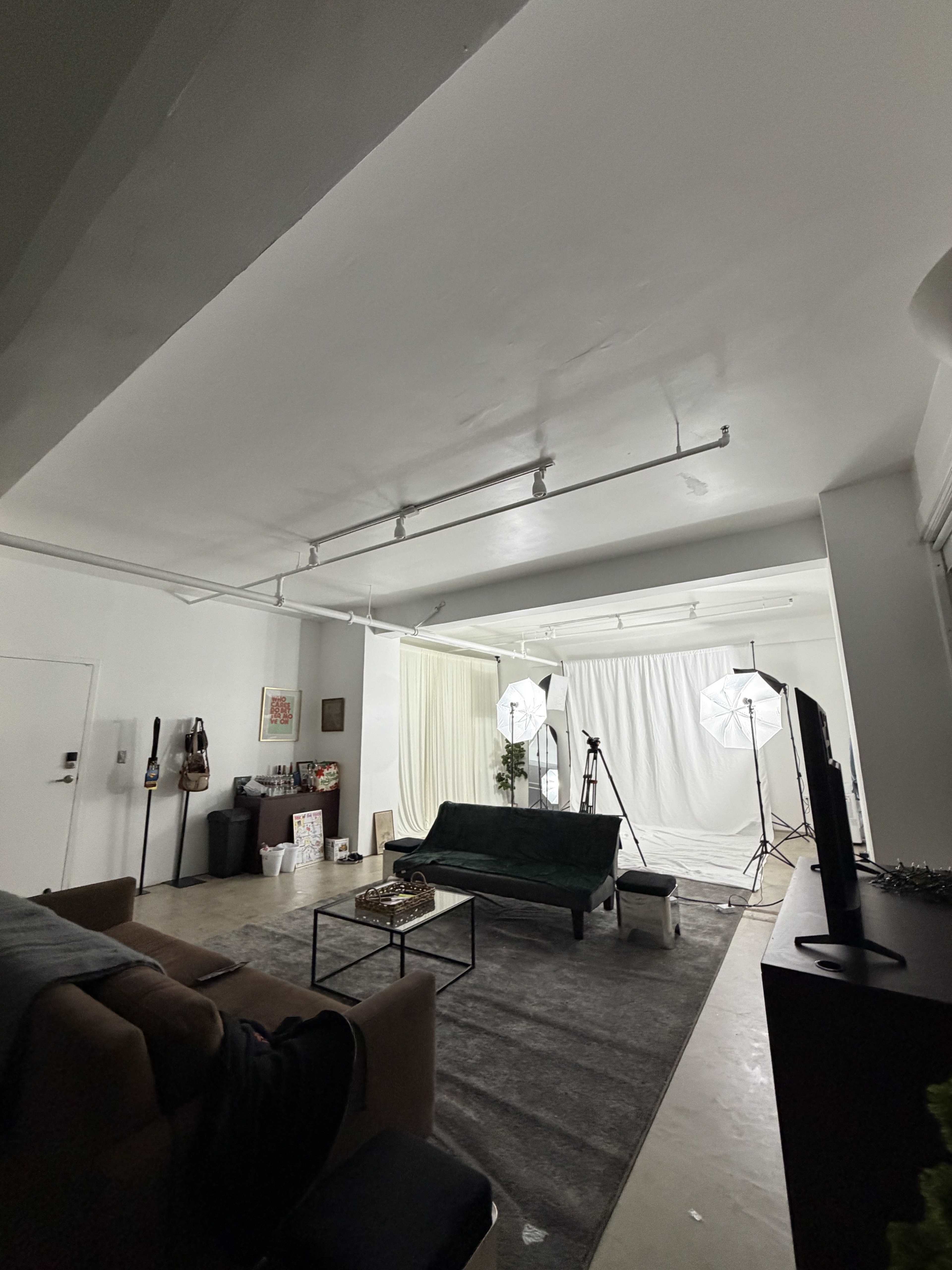 The image shows a studio space equipped with two lighting setups, a green couch, and a white backdrop, alongside various props and a dark rug on the floor.