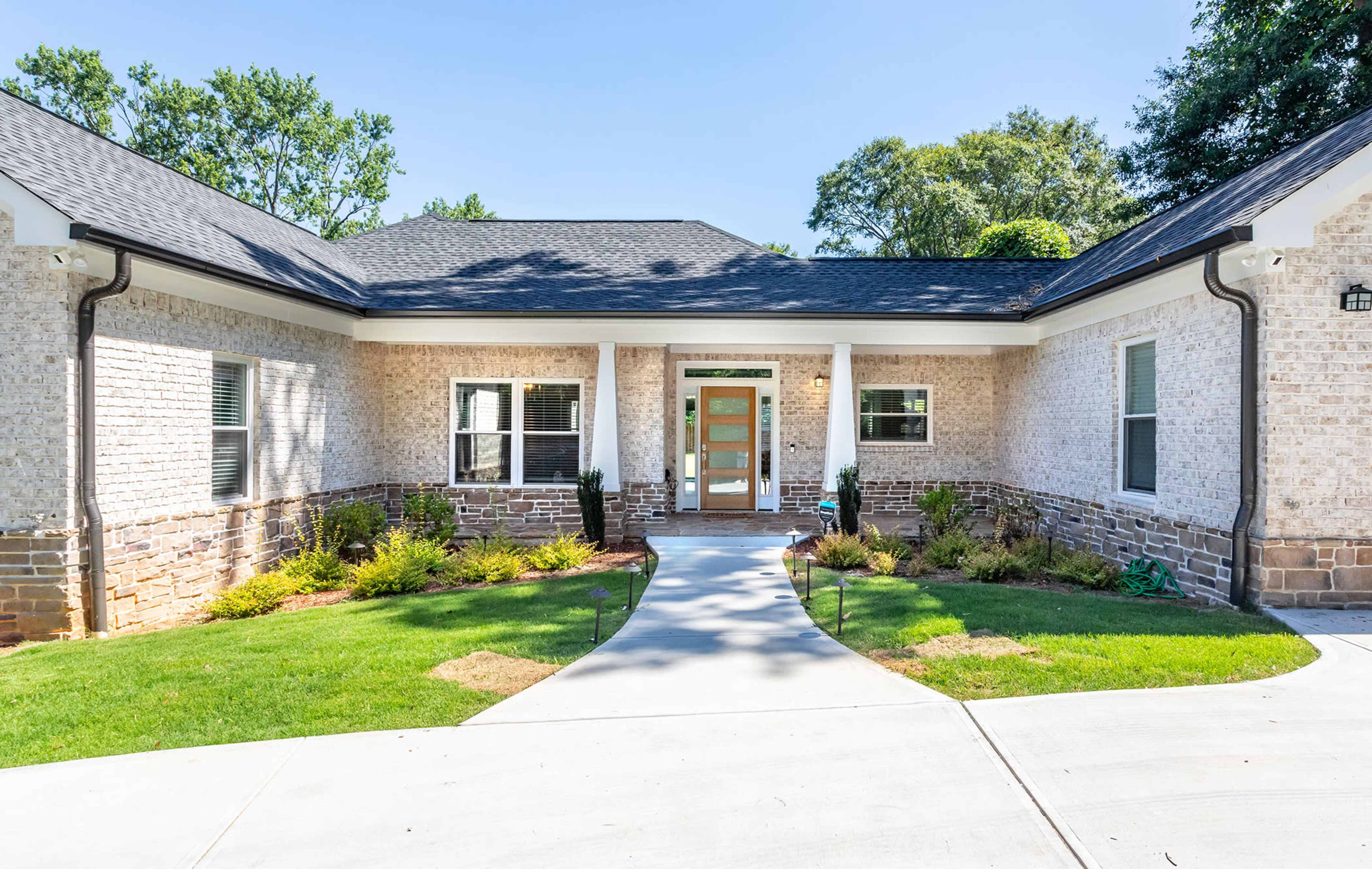 A single-story brick house with a landscaped front yard and a concrete pathway leading to the entrance.