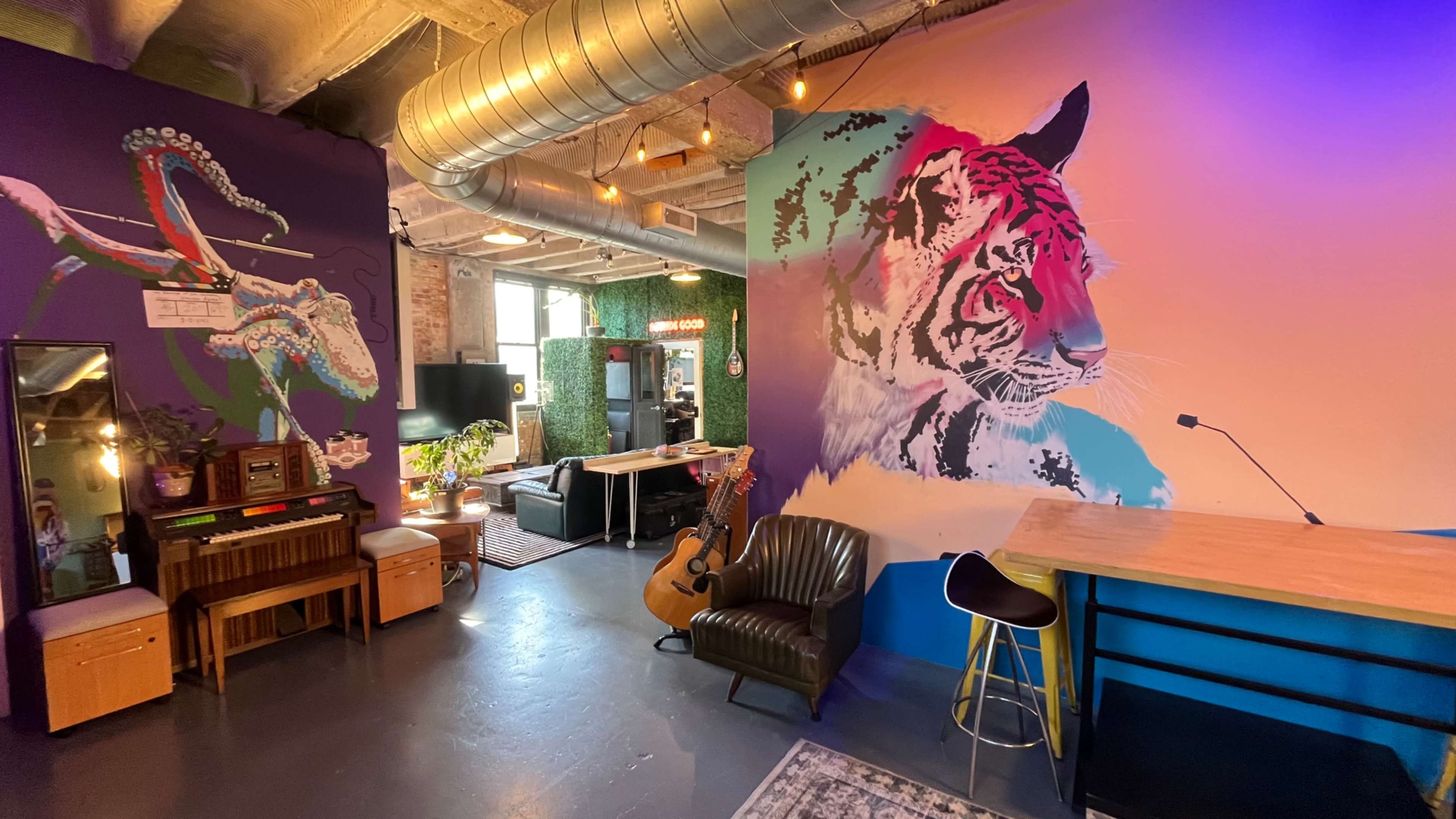 The image shows a vibrant room featuring colorful wall murals of a tiger and a bird, with a mix of seating arrangements, a guitar, and various decor elements.
