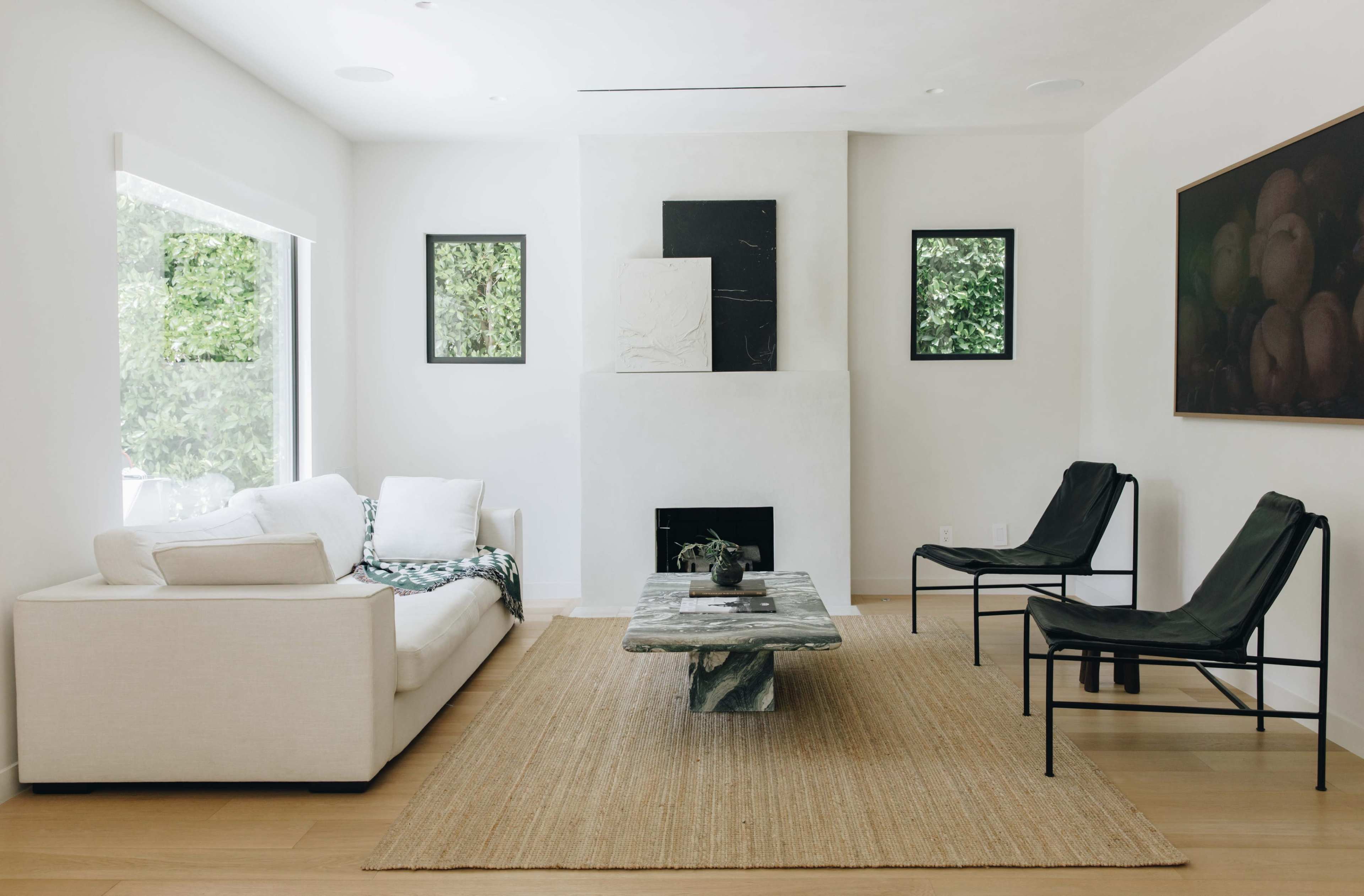 A minimalist living room features a white sofa, a black coffee table, two black chairs, and artwork on the walls.