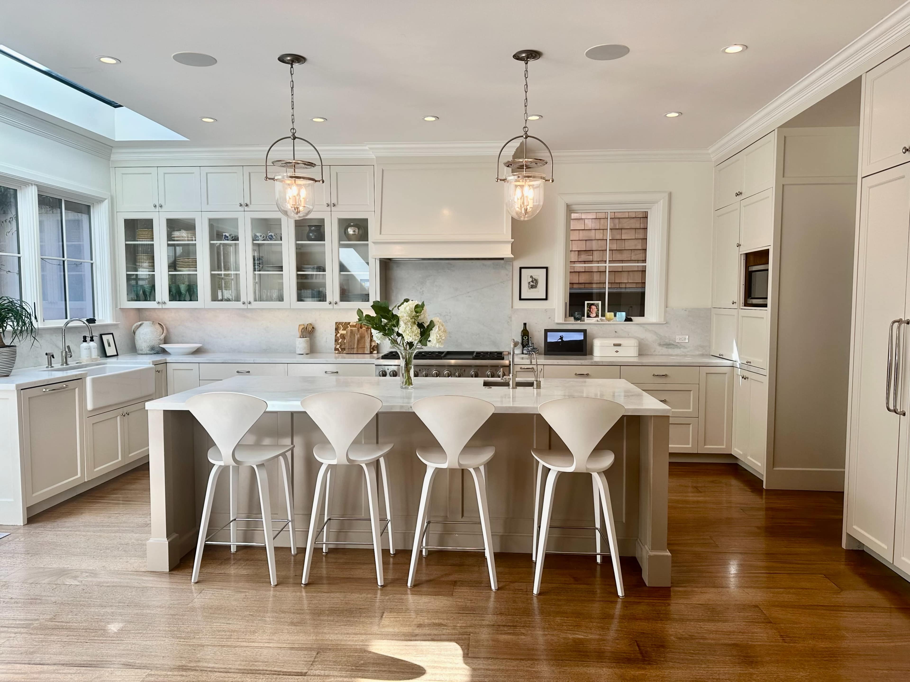 The image shows a modern kitchen featuring white cabinetry, a central island with seating for four, and pendant lights above the island.