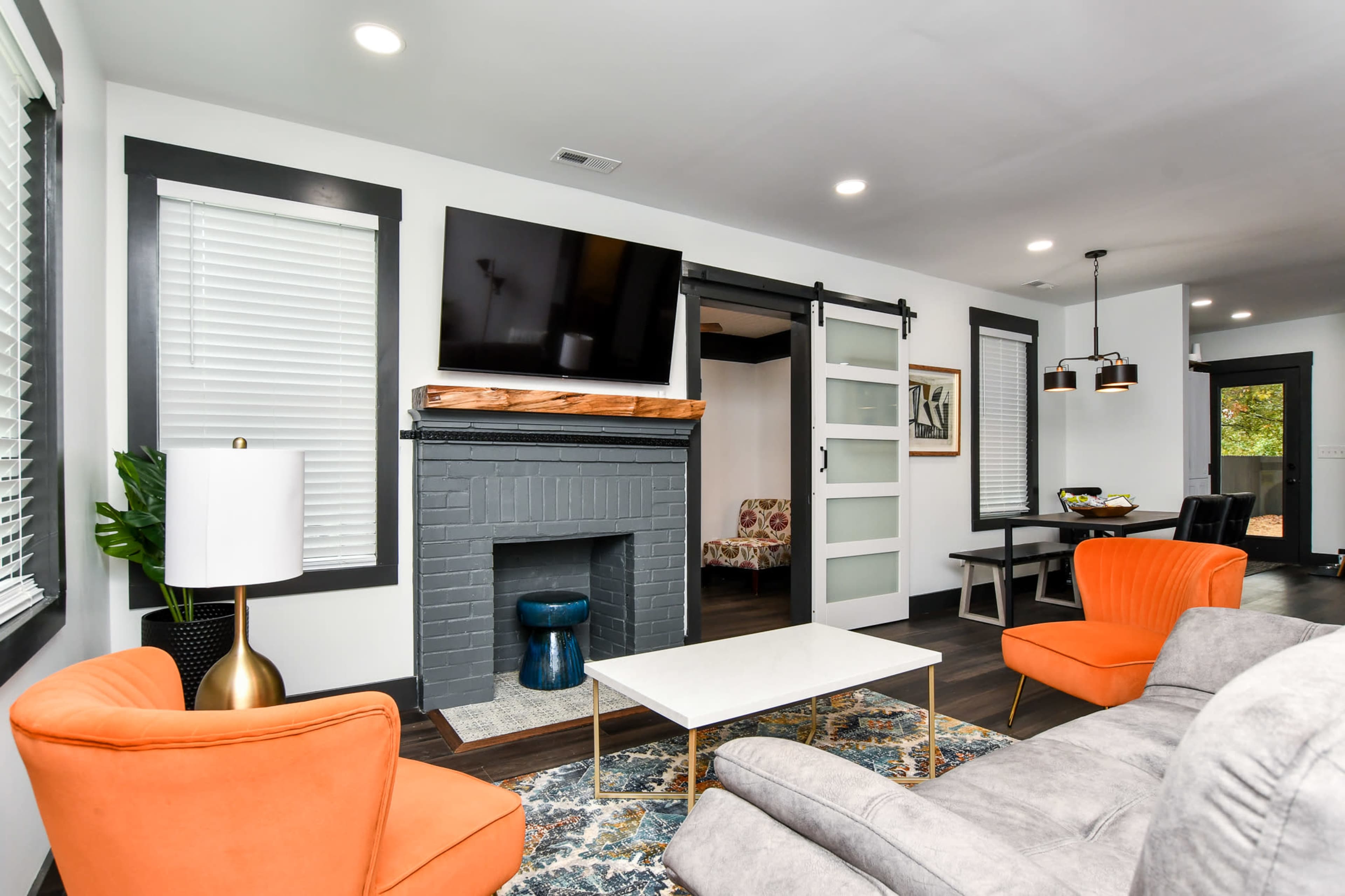 The living room features orange armchairs, a gray brick fireplace, a wall-mounted television, and a sliding glass door leading to another room.
