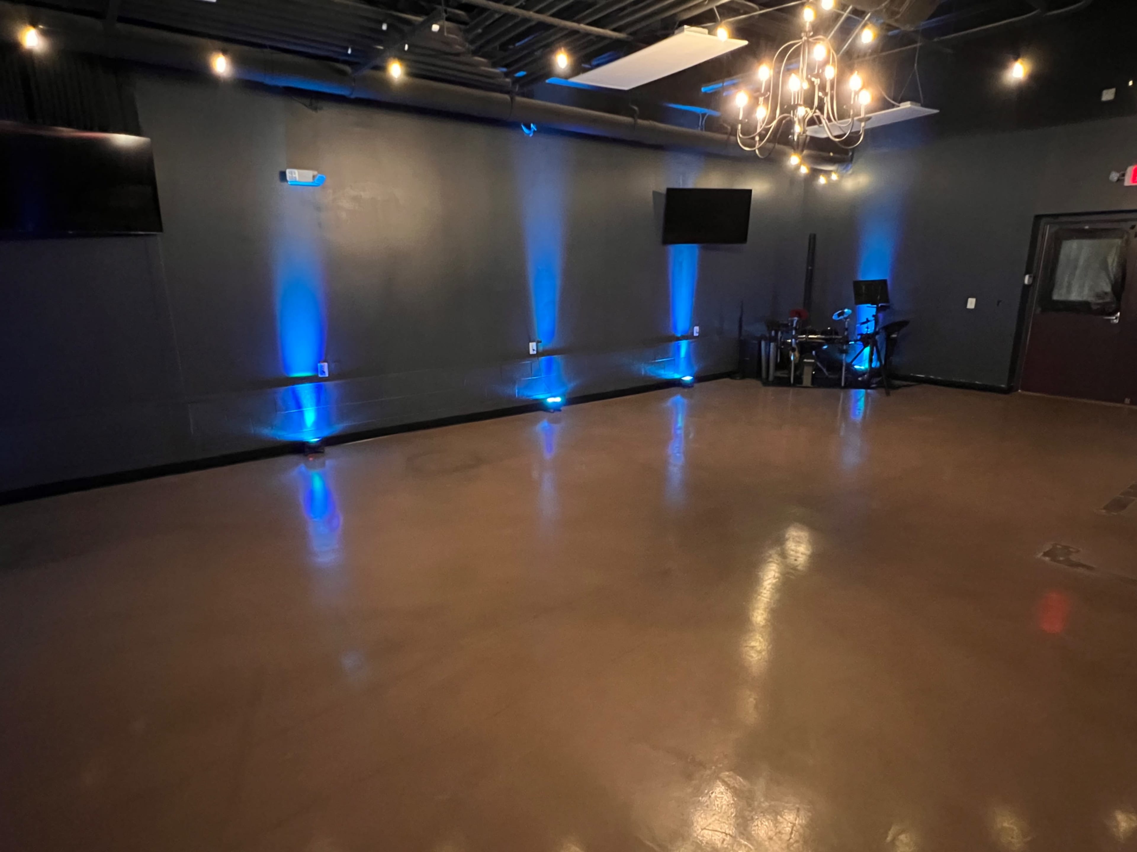 A spacious, dimly lit room with a polished floor, blue LED lighting along the walls, and two wall-mounted TVs.
