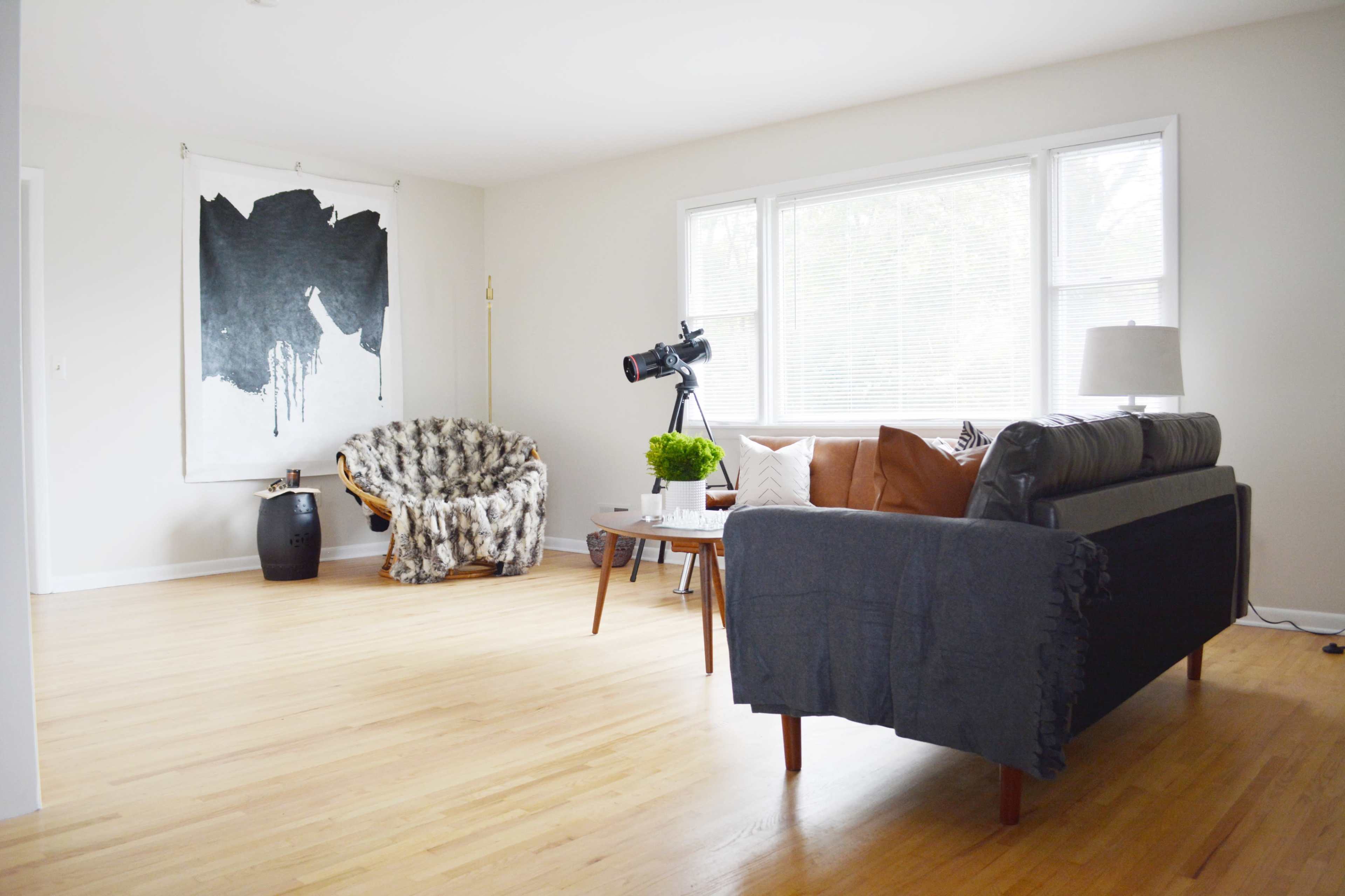 The room features a sofa with a throw, a round coffee table, a large piece of abstract artwork on the wall, and a telescope positioned beside a window.
