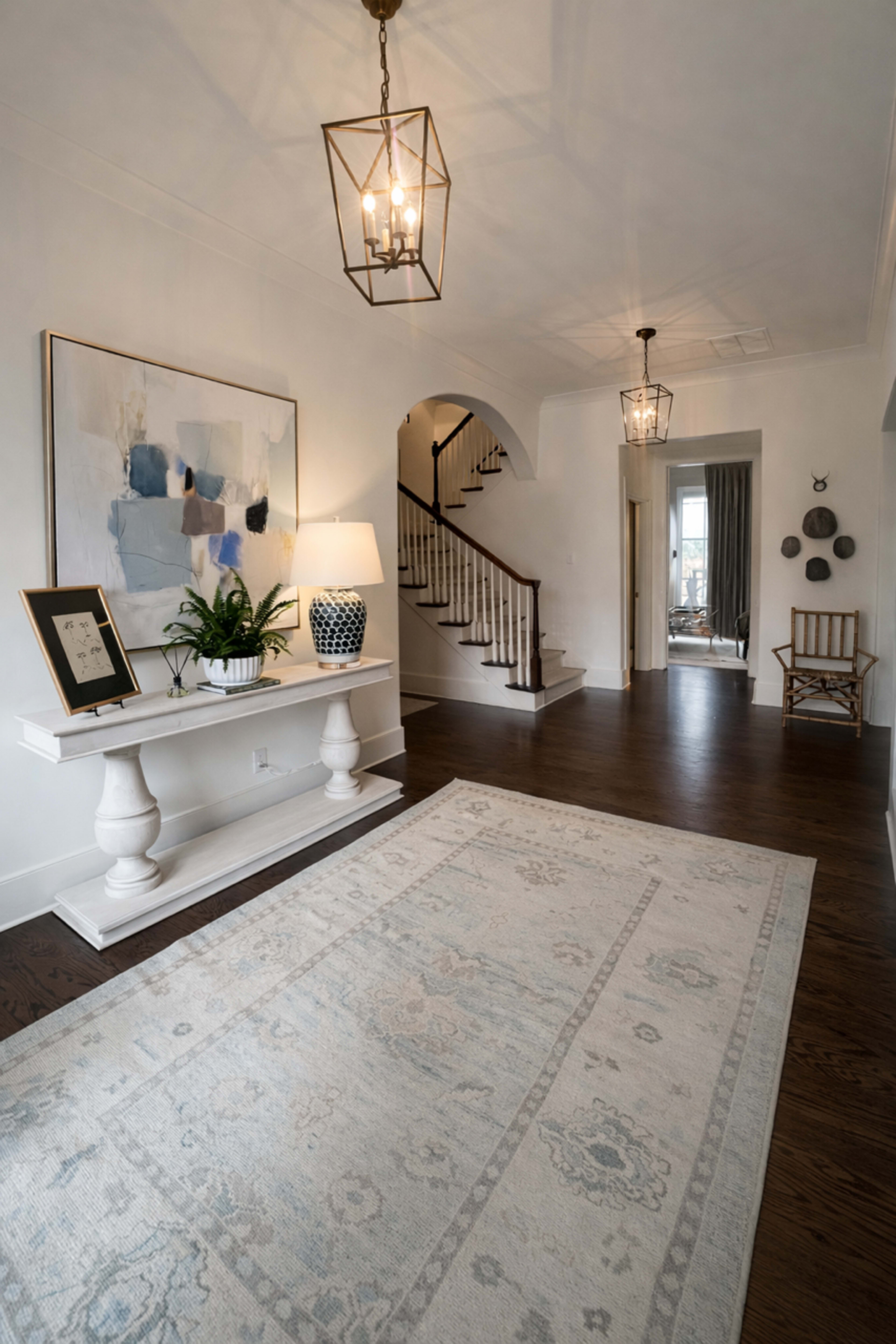 The image depicts a spacious entryway with a decorative console table, a large artwork on the wall, and a staircase leading to the upper level.